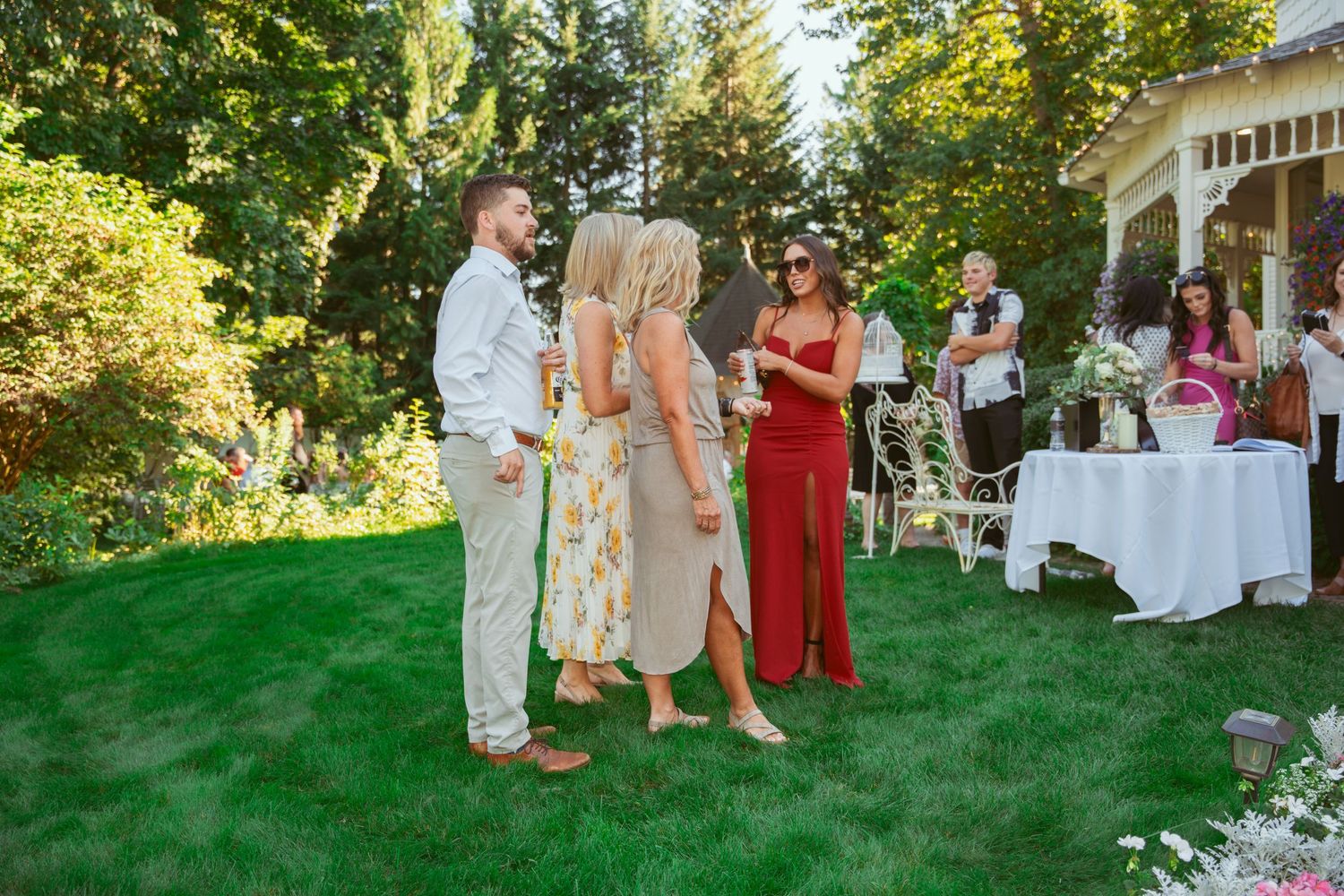 Wedding party members in formal attire gather on a lush green lawn during an outdoor summer celebration.