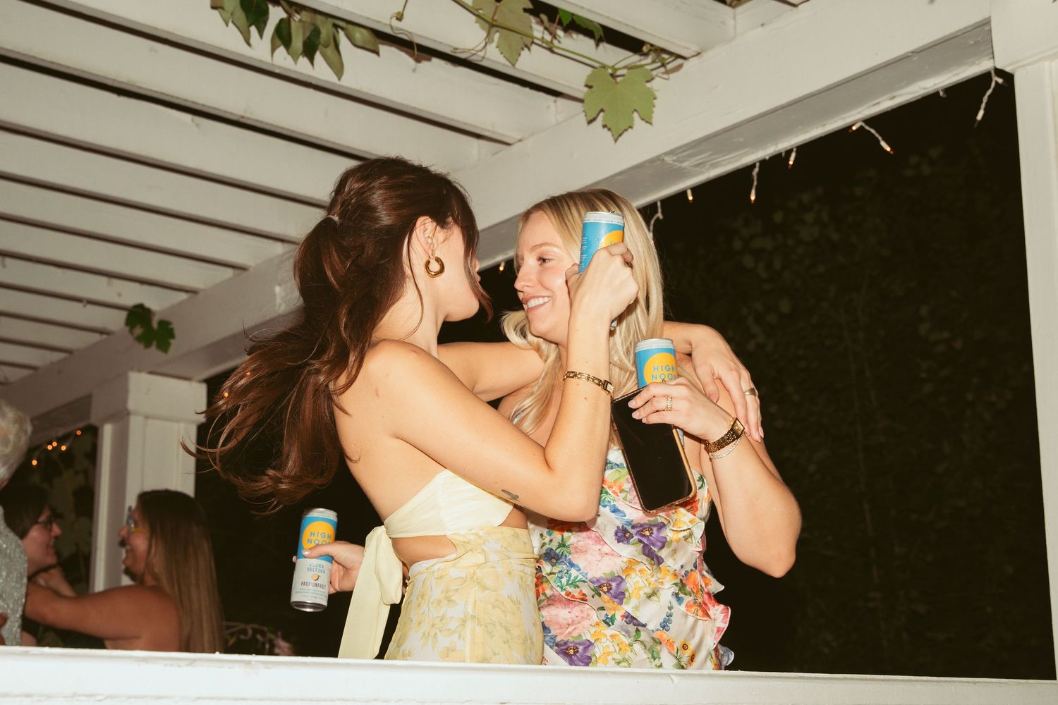 Wedding guests enjoying drinks and dancing at outdoor reception under covered patio.