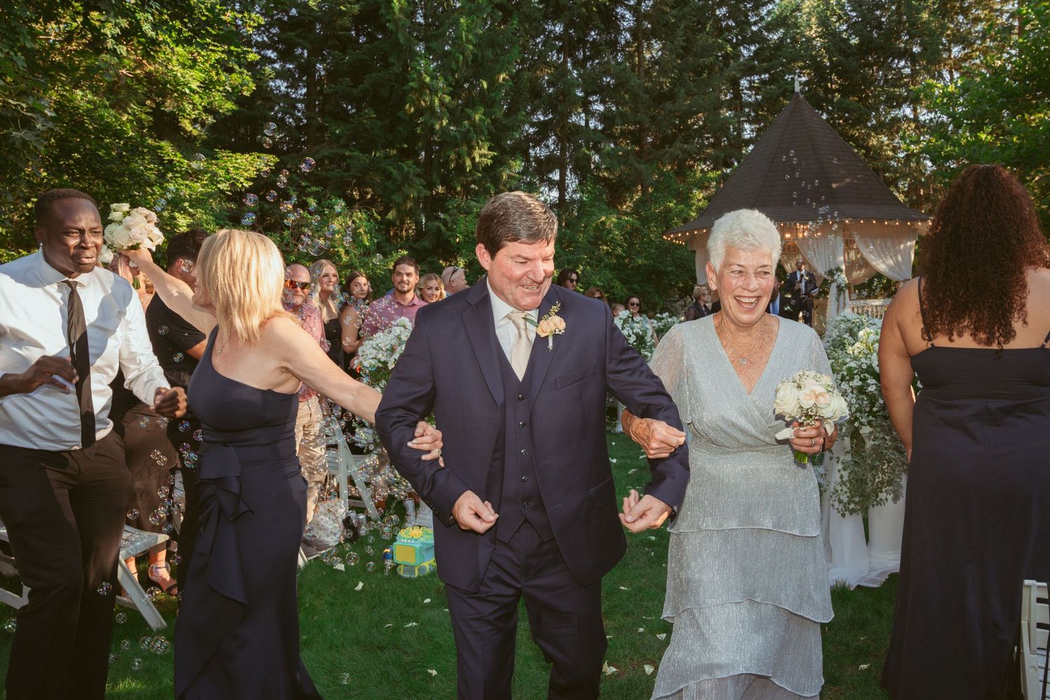 Wedding party dances in a line formation during an outdoor garden celebration.