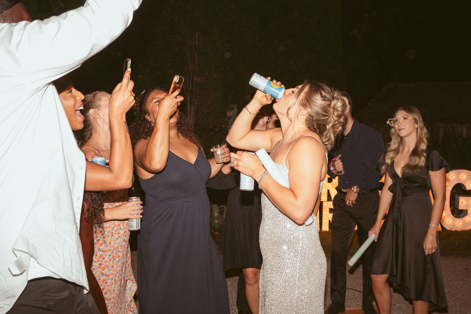 Wedding guests dance and celebrate on a dimly lit dance floor at an evening reception.