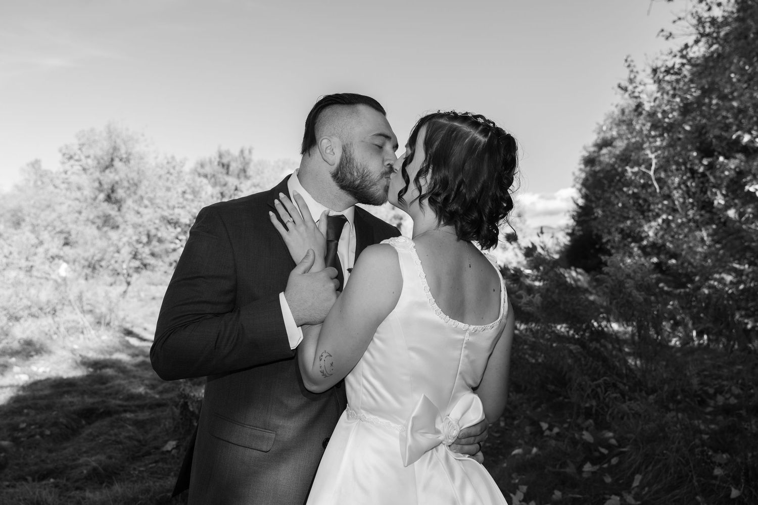 A black and white wedding portrait capturing a tender moment between newlyweds outdoors.