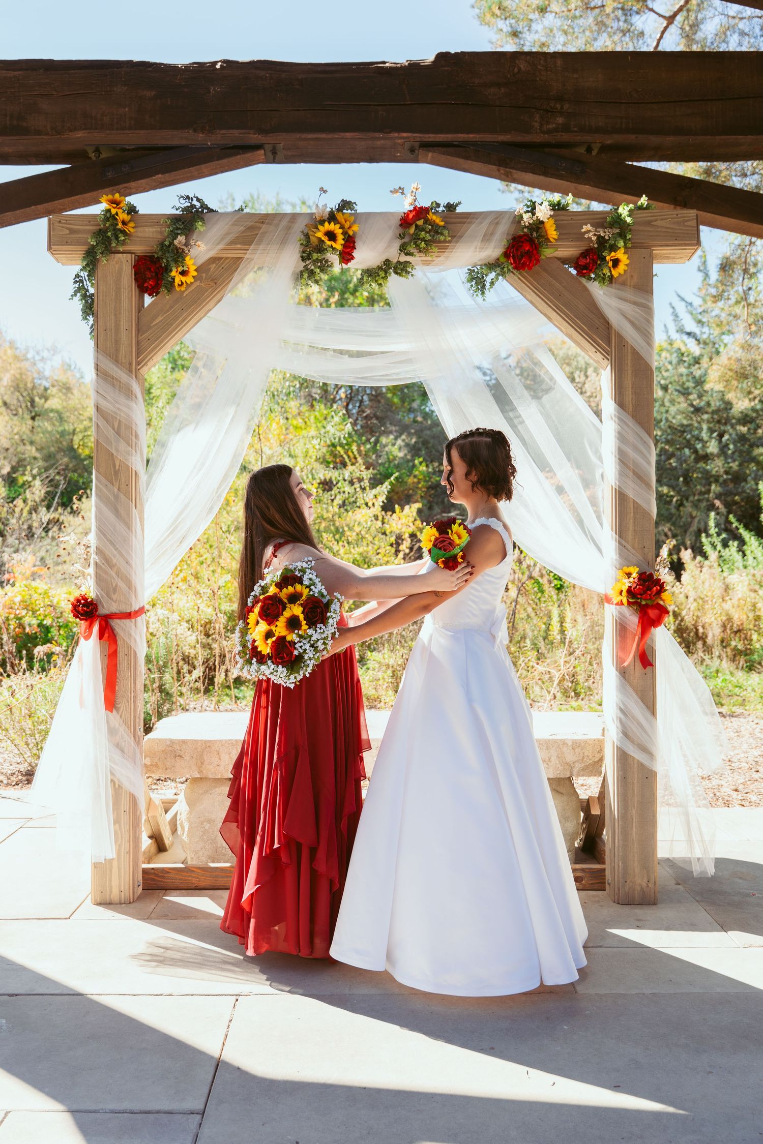 Wedding party members pose in red and white attire under decorated outdoor pavilion.