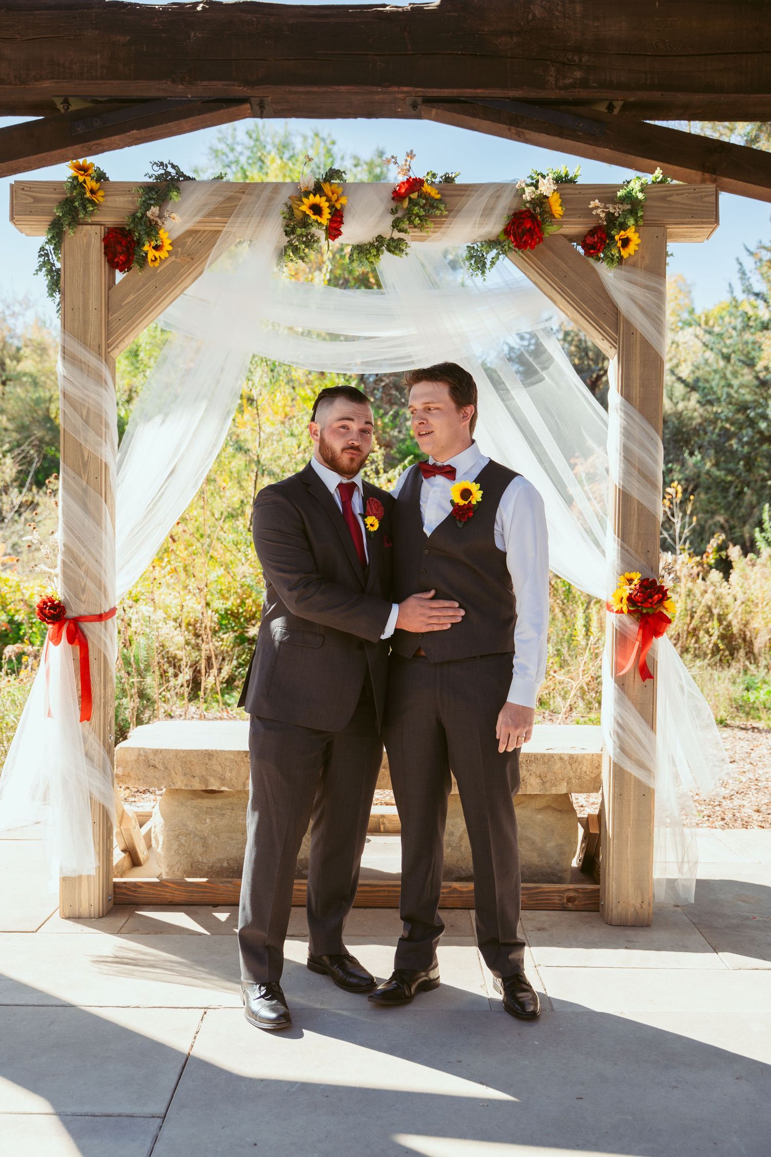 Wedding party members share emotional moments under decorated outdoor pavilion.