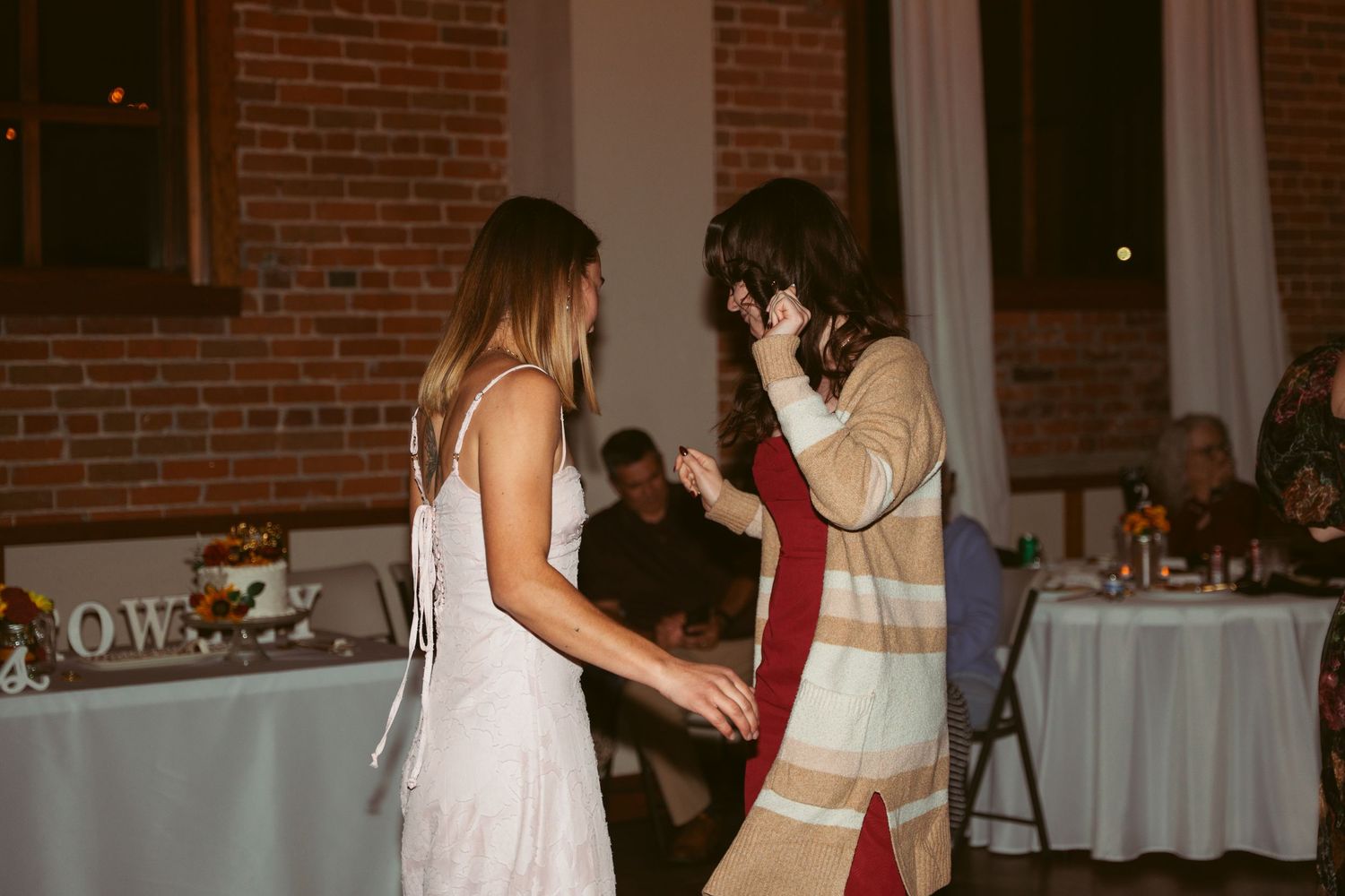 Wedding guests dancing together at reception in front of exposed brick walls.