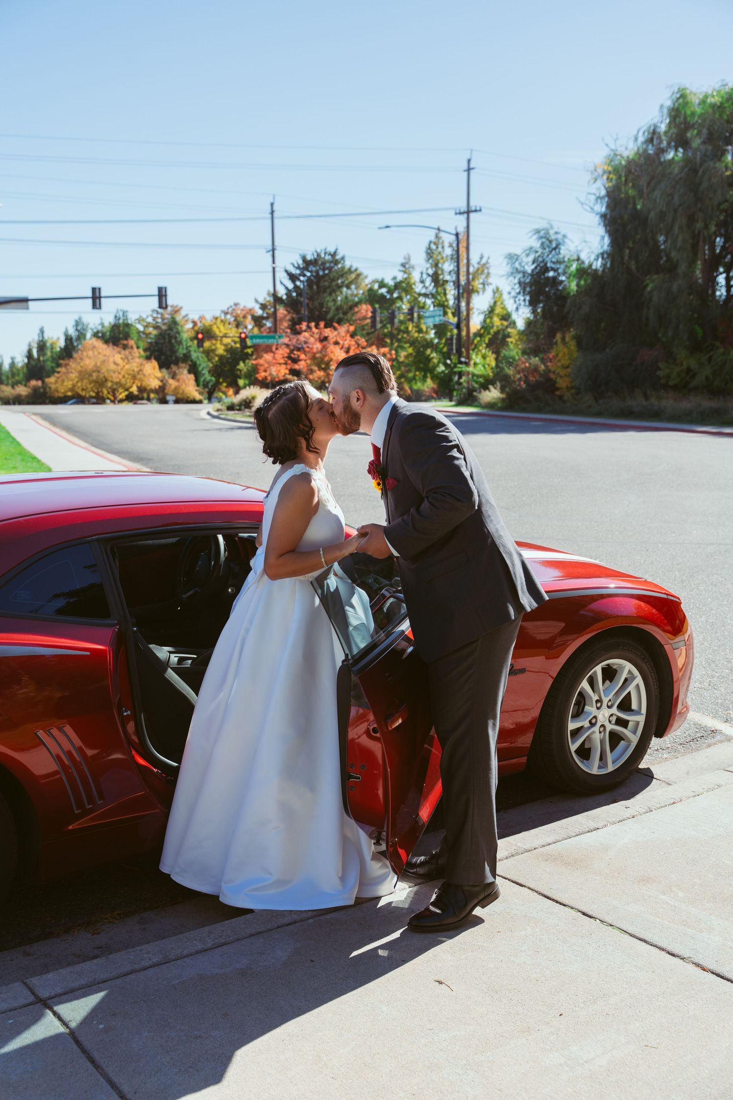 A romantic moment captured beside a red car during a wedding photoshoot.