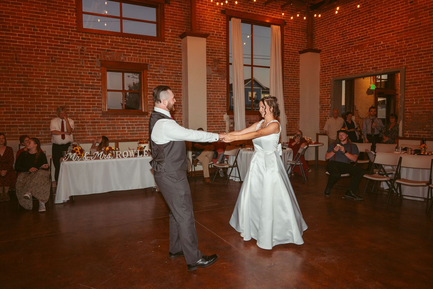 Dancers perform an elegant twirl in a spacious brick-walled reception space with decorative lighting.