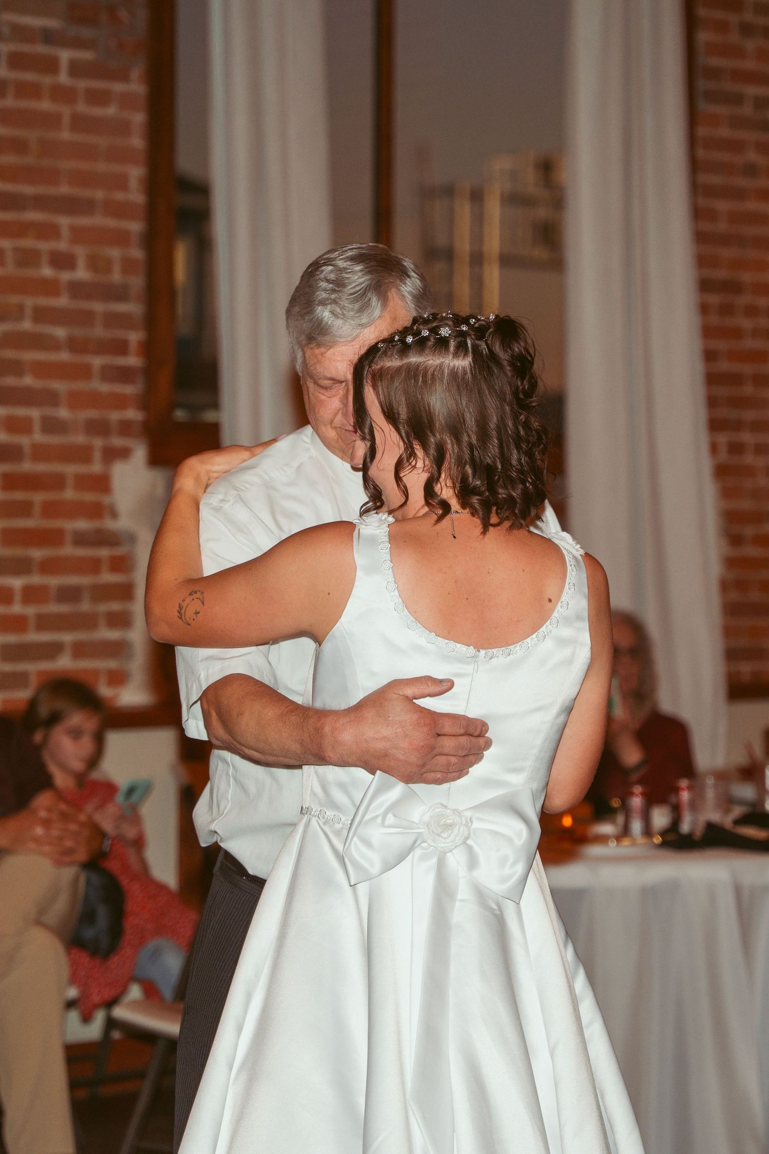 A heartfelt slow dance moment at a wedding reception with brick walls and white decor.