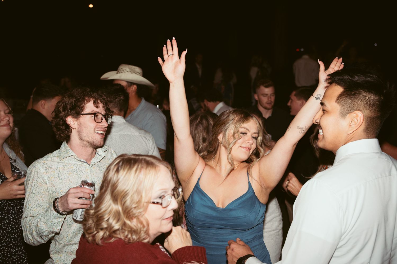 Wedding guests dancing and celebrating on a wooden dance floor under string lights.