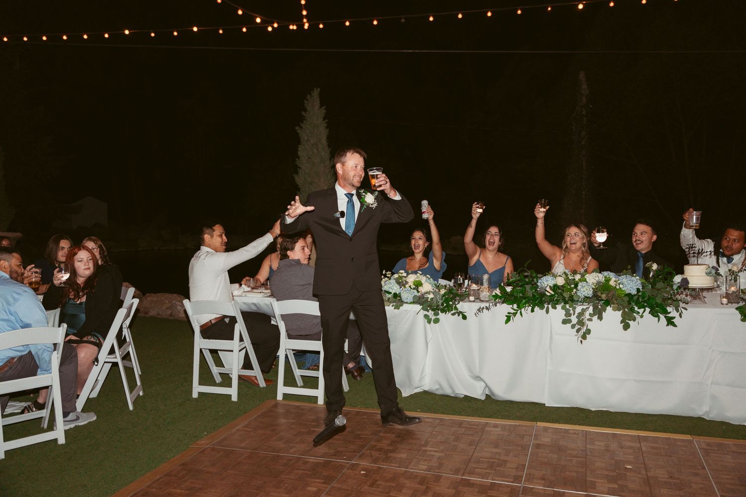 Wedding guests dance and celebrate during an outdoor evening reception under string lights.
