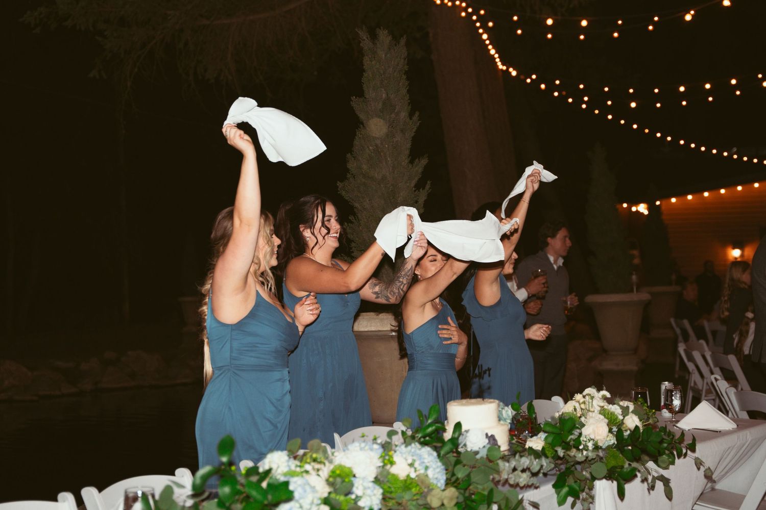 Wedding guests dance under twinkling string lights at an outdoor evening celebration.