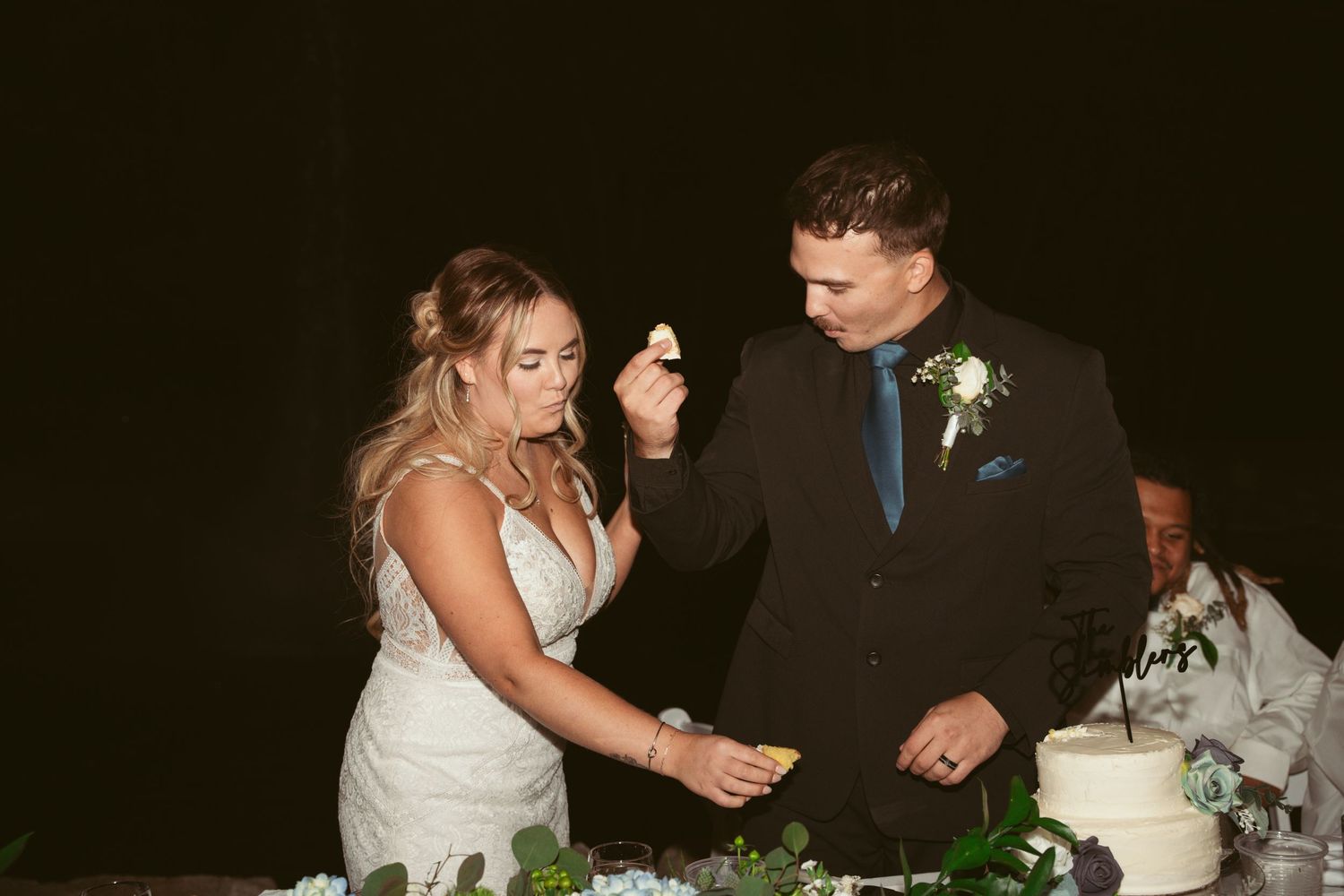 A couple dances together at an outdoor evening wedding reception with string lights overhead.