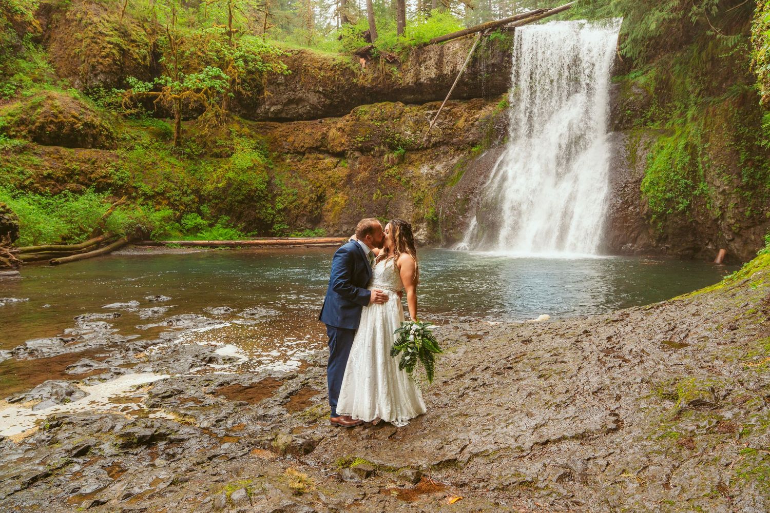 Couple poses for romantic wedding photos near majestic forest waterfall.