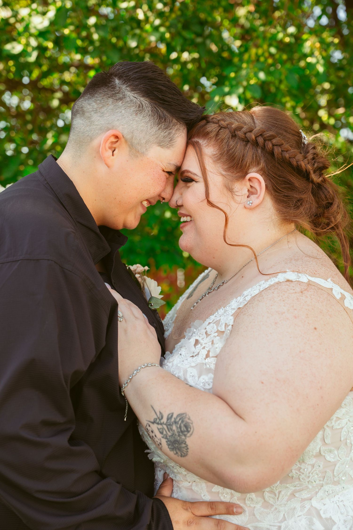 Tender wedding moment captured in a lush garden setting with delicate lace dress details.
