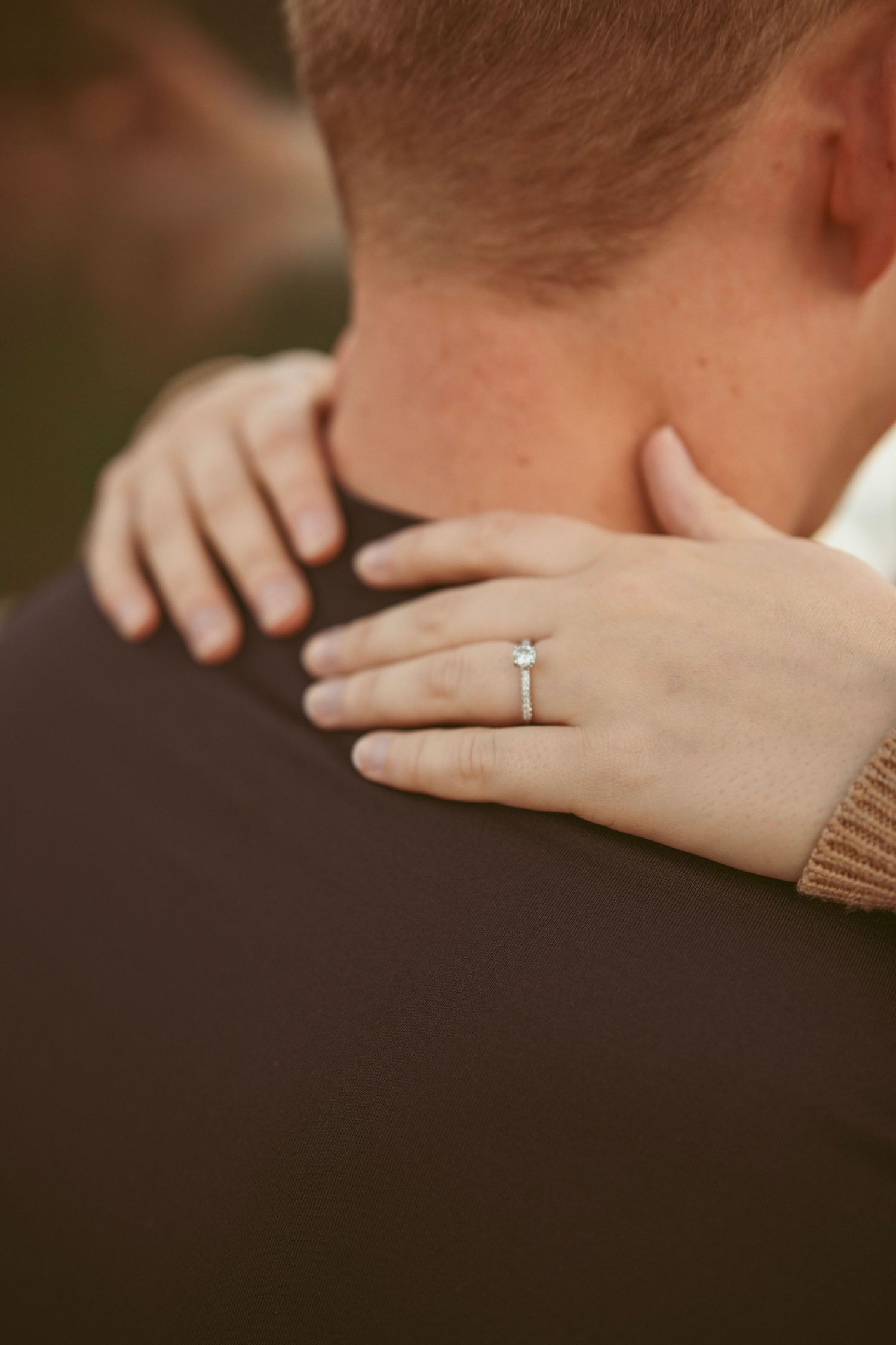 Close-up shot of hands with delicate tattoos and an engagement ring against a dark background.