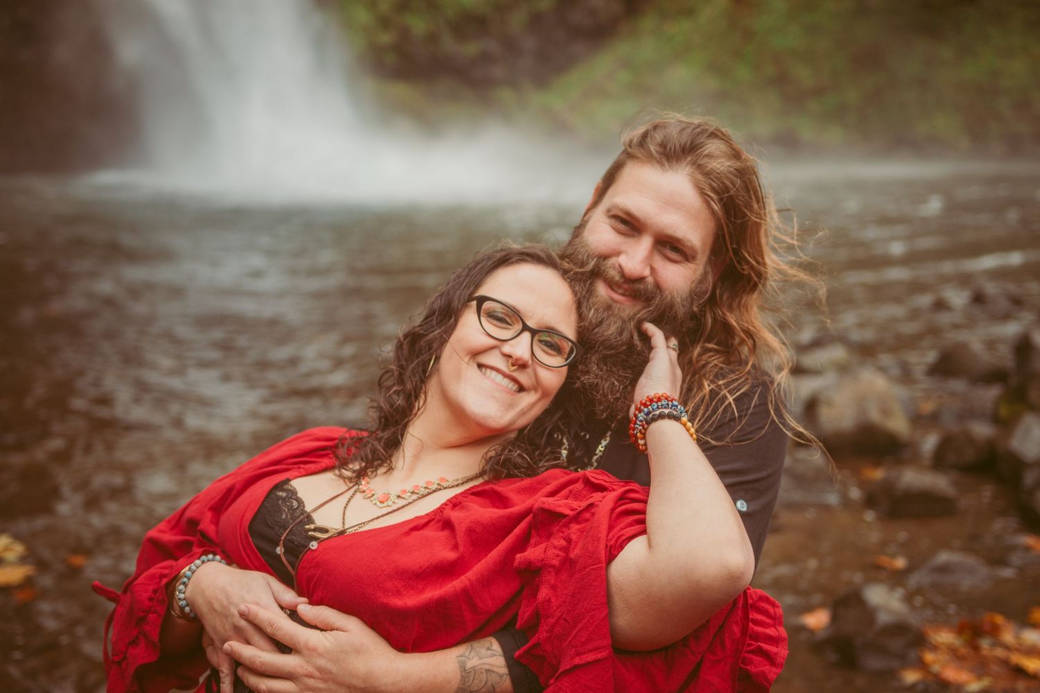 Couple shares an intimate moment by a waterfall with autumn foliage in the background.