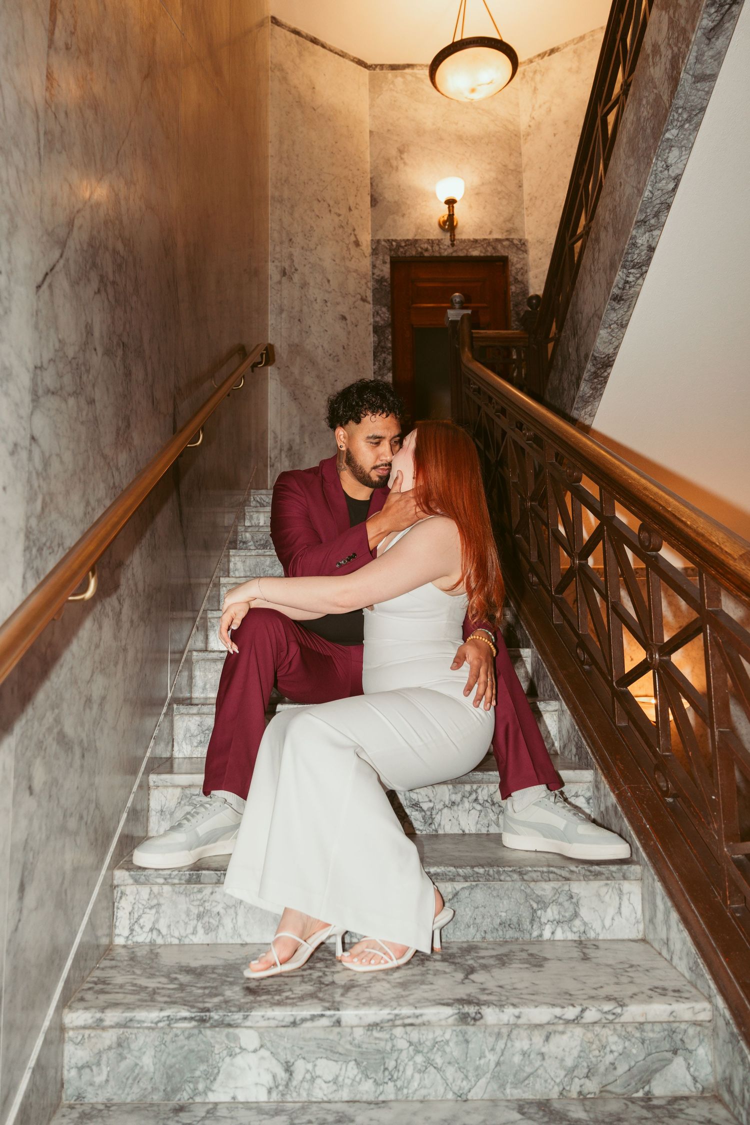 A couple sits close together on marble stairs in an elegant indoor setting.