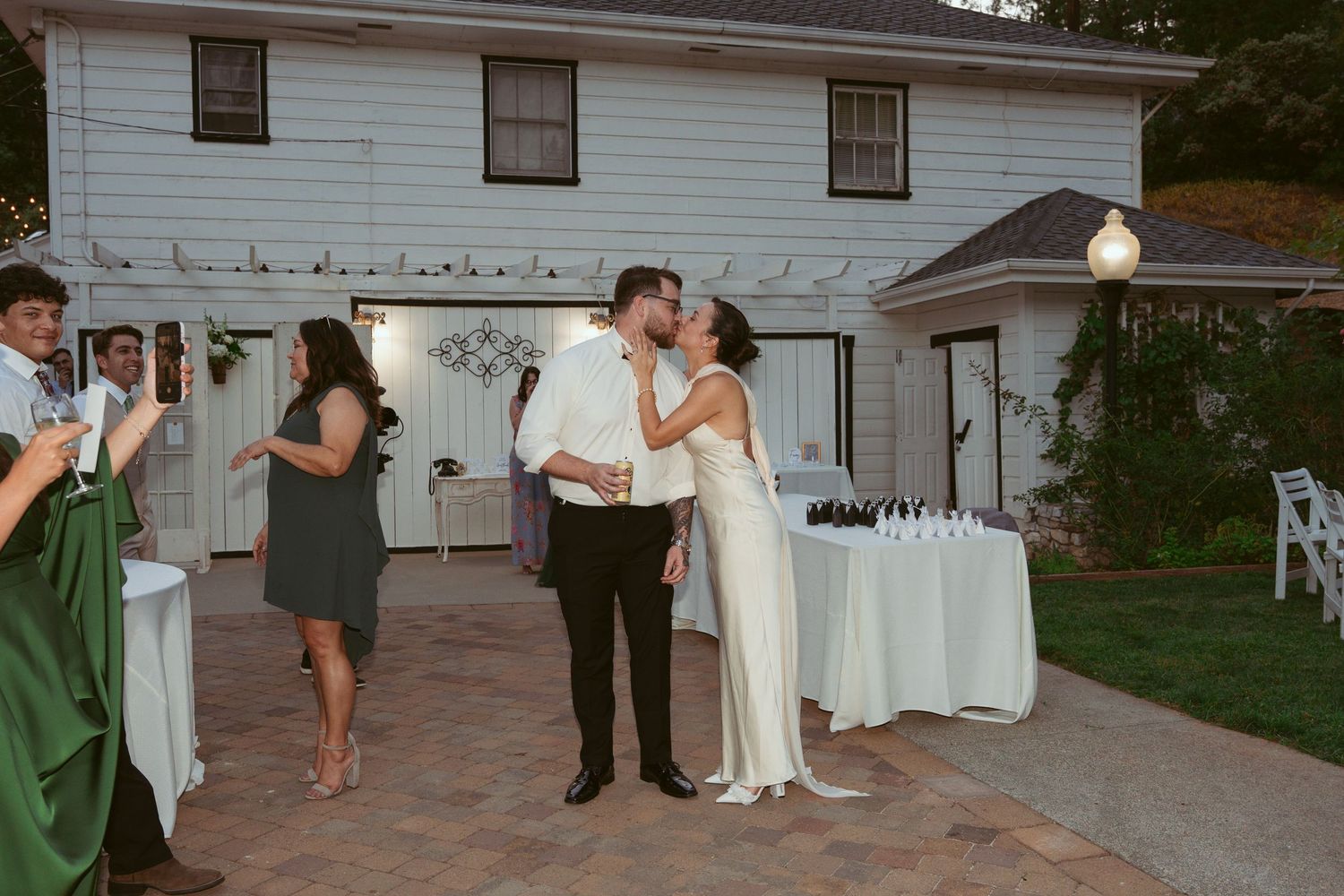 A couple shares a romantic moment near their wedding cake table at dusk.