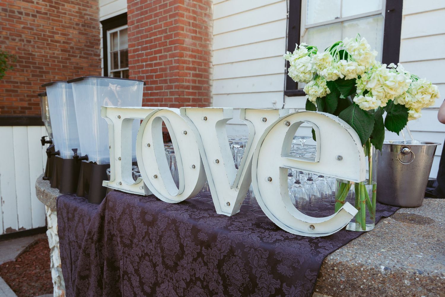 White decorative LOVE letters displayed on a dark tablecloth with floral arrangements.