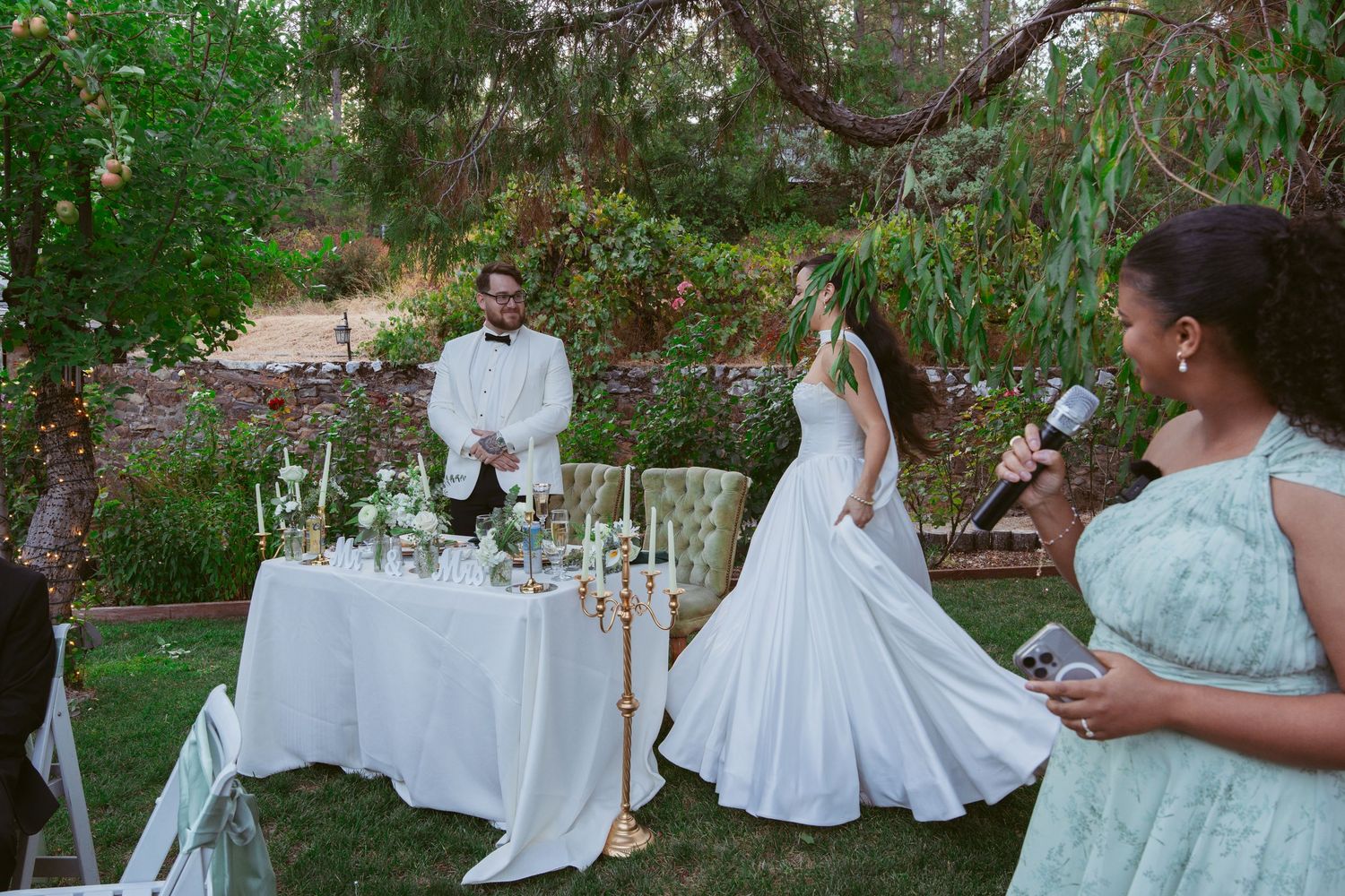 Outdoor garden wedding reception with white tables set under green trees.