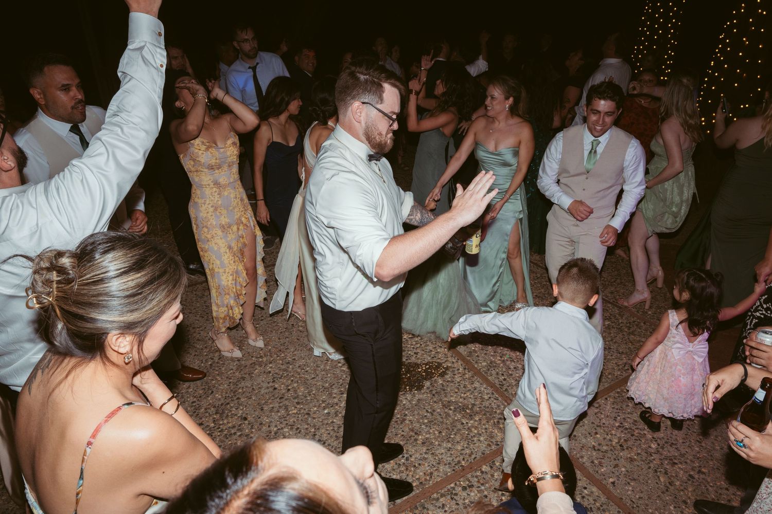 Wedding guests dancing and celebrating on an outdoor dance floor at night under string lights.