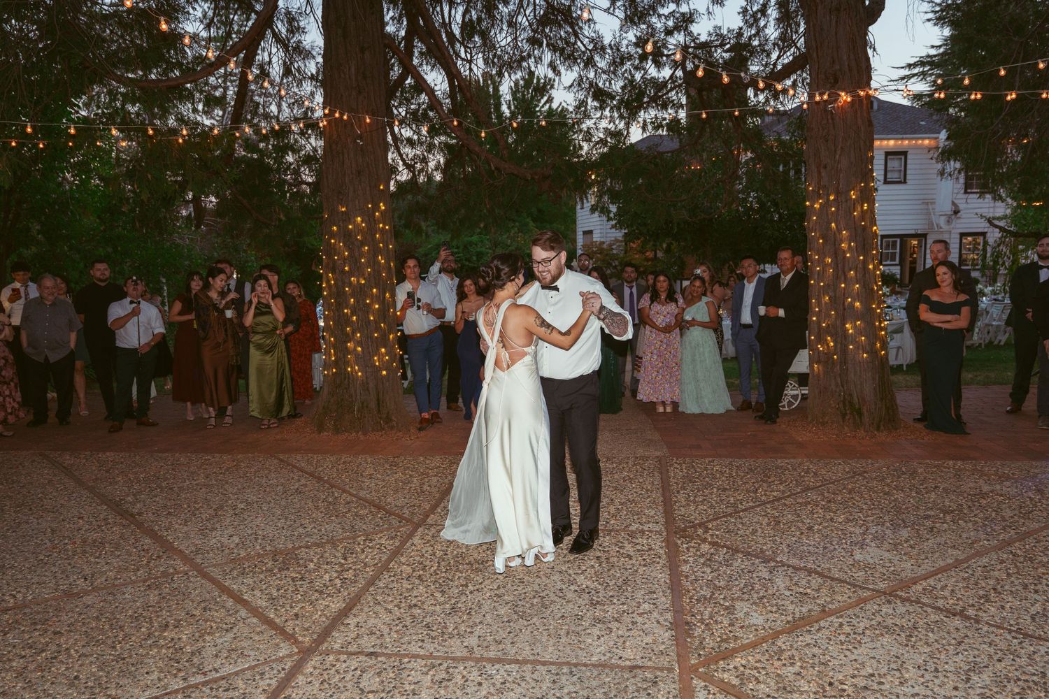 Outdoor wedding reception dance floor under trees with string lights creating a romantic atmosphere.