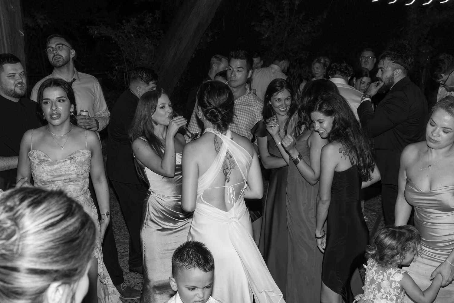 Black and white photo of wedding guests dancing and celebrating at an evening reception.