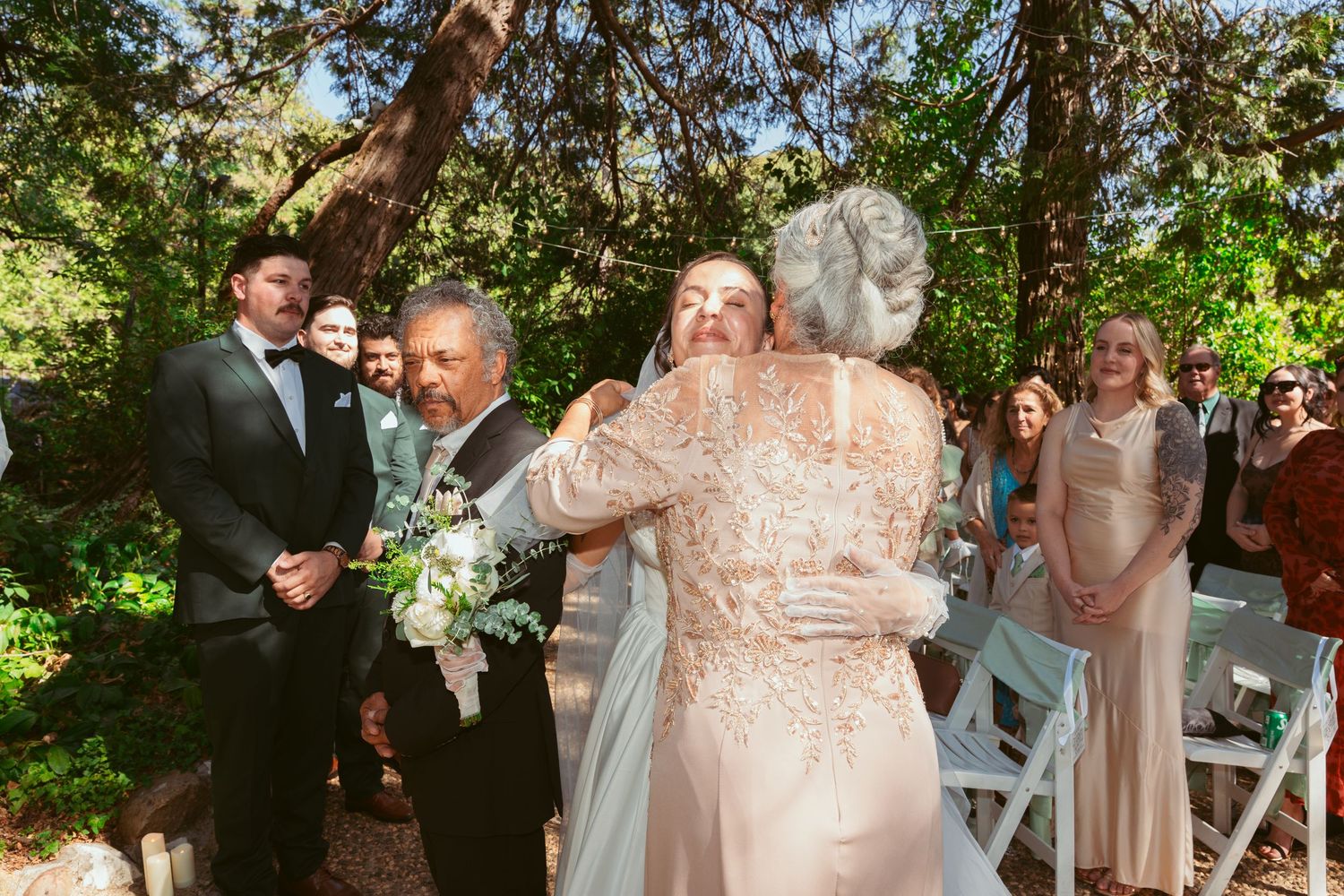 Wedding ceremony guests gather under trees for outdoor celebration.