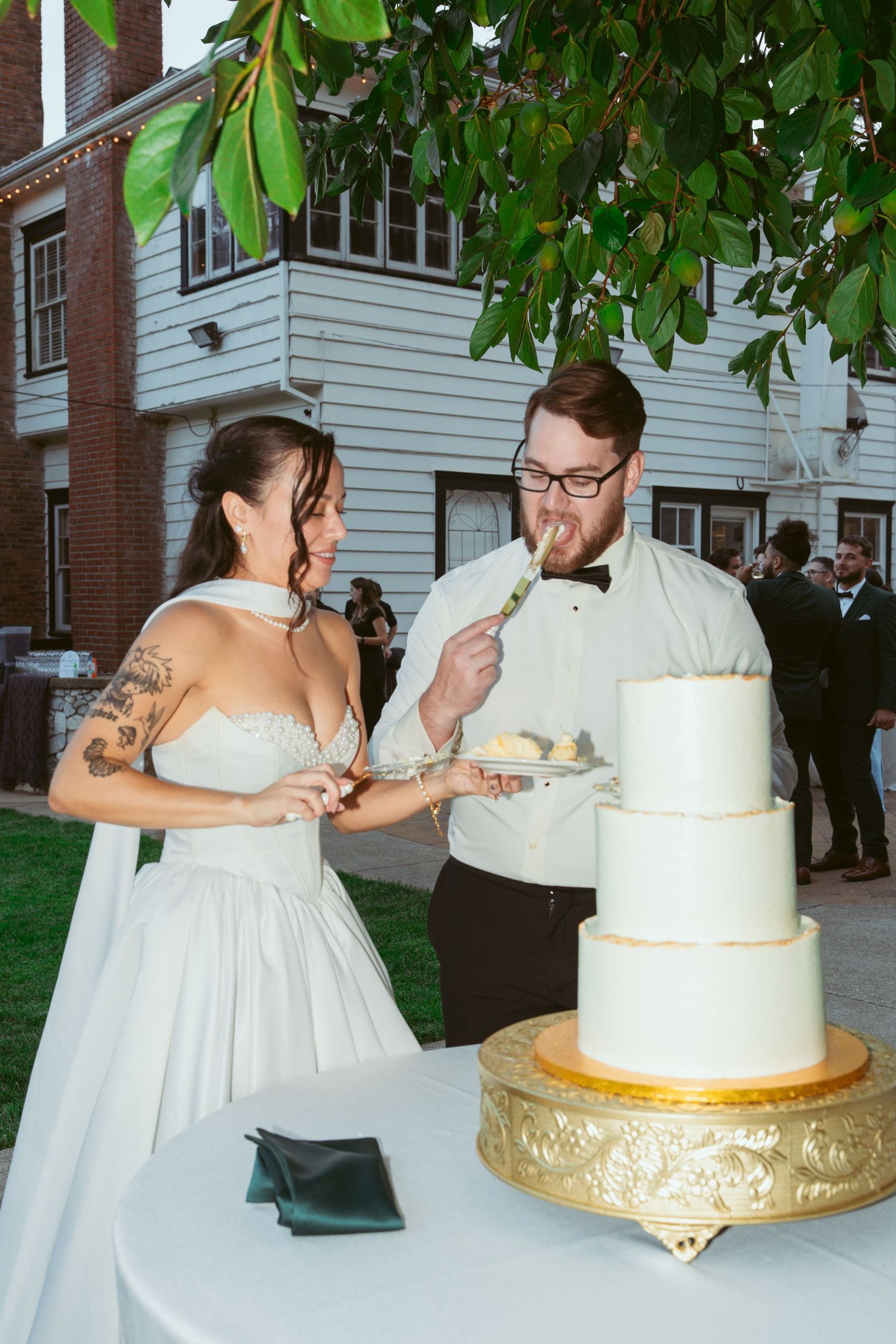 A couple cutting their elegant white and gold wedding cake together during their outdoor reception.