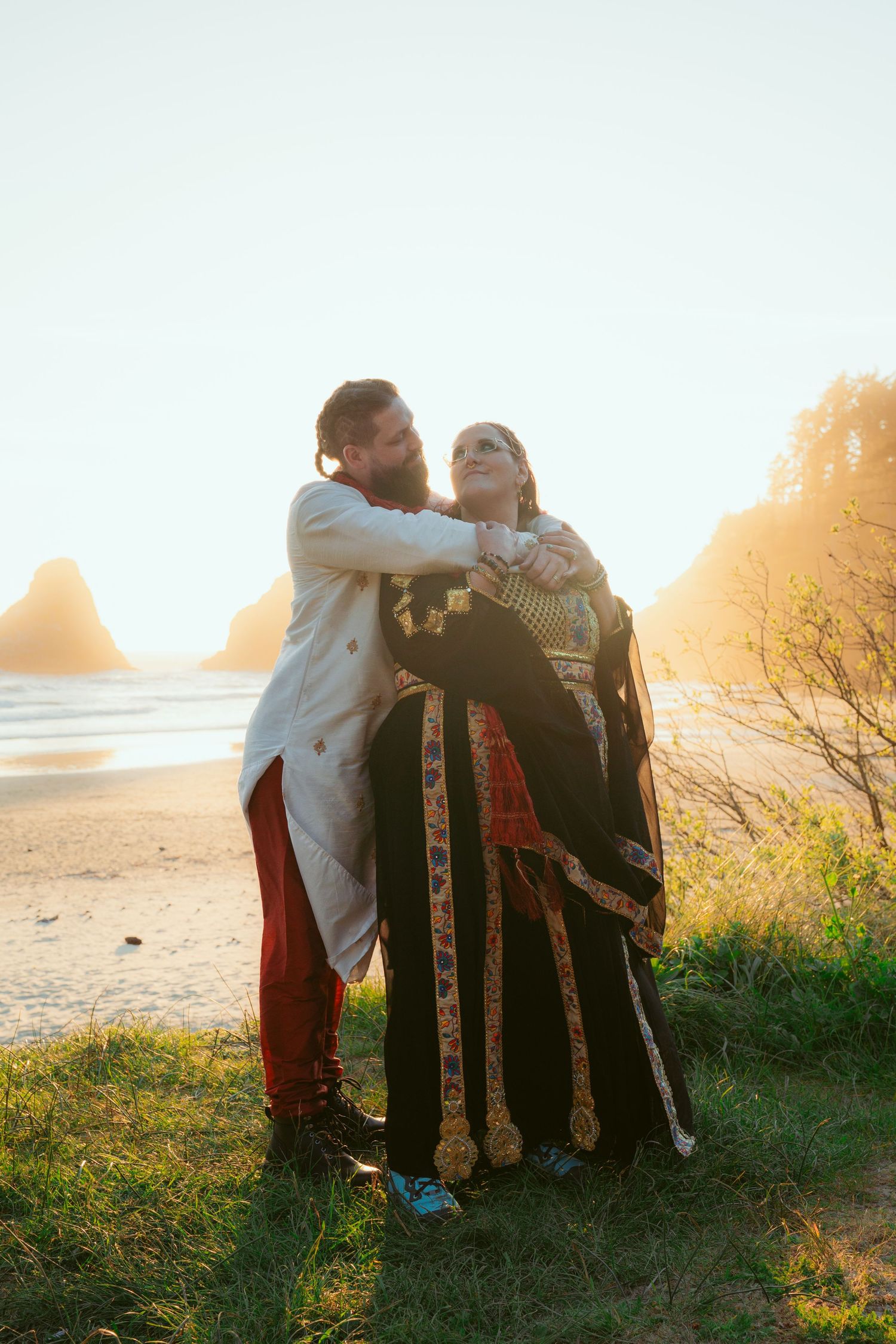 Romantic couple shares tender moment on grassy hillside overlooking ocean at golden hour.