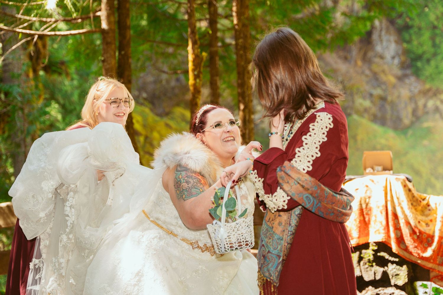 Wedding participants in medieval-themed attire interact during an outdoor forest ceremony.