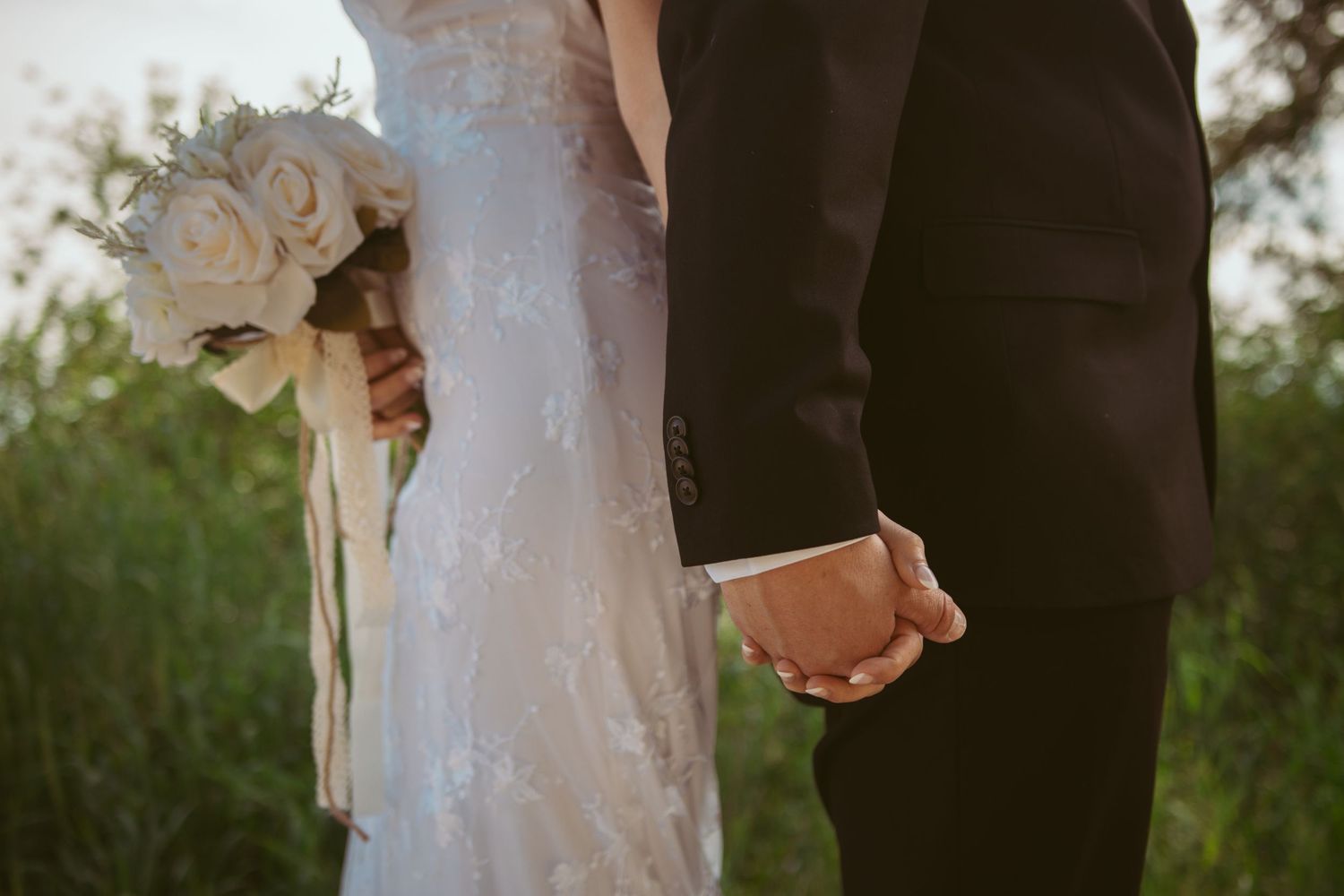 A close-up detail shot of hands and a white bouquet during a wedding ceremony.