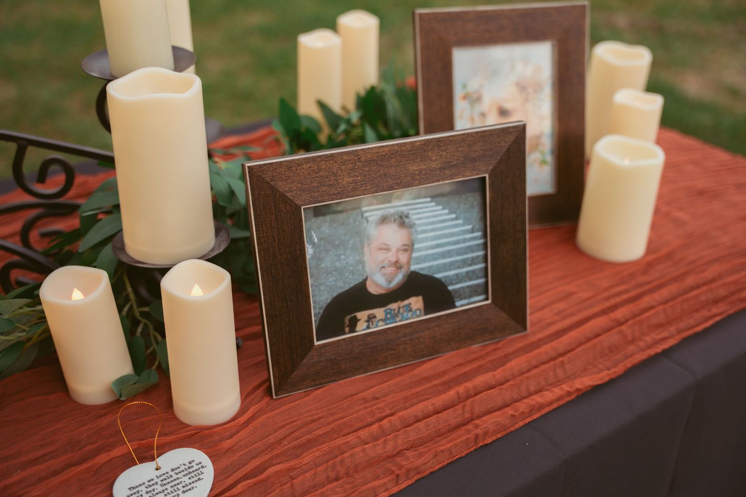 Memorial display with framed photos, white candles, and decorative elements on a red tablecloth.