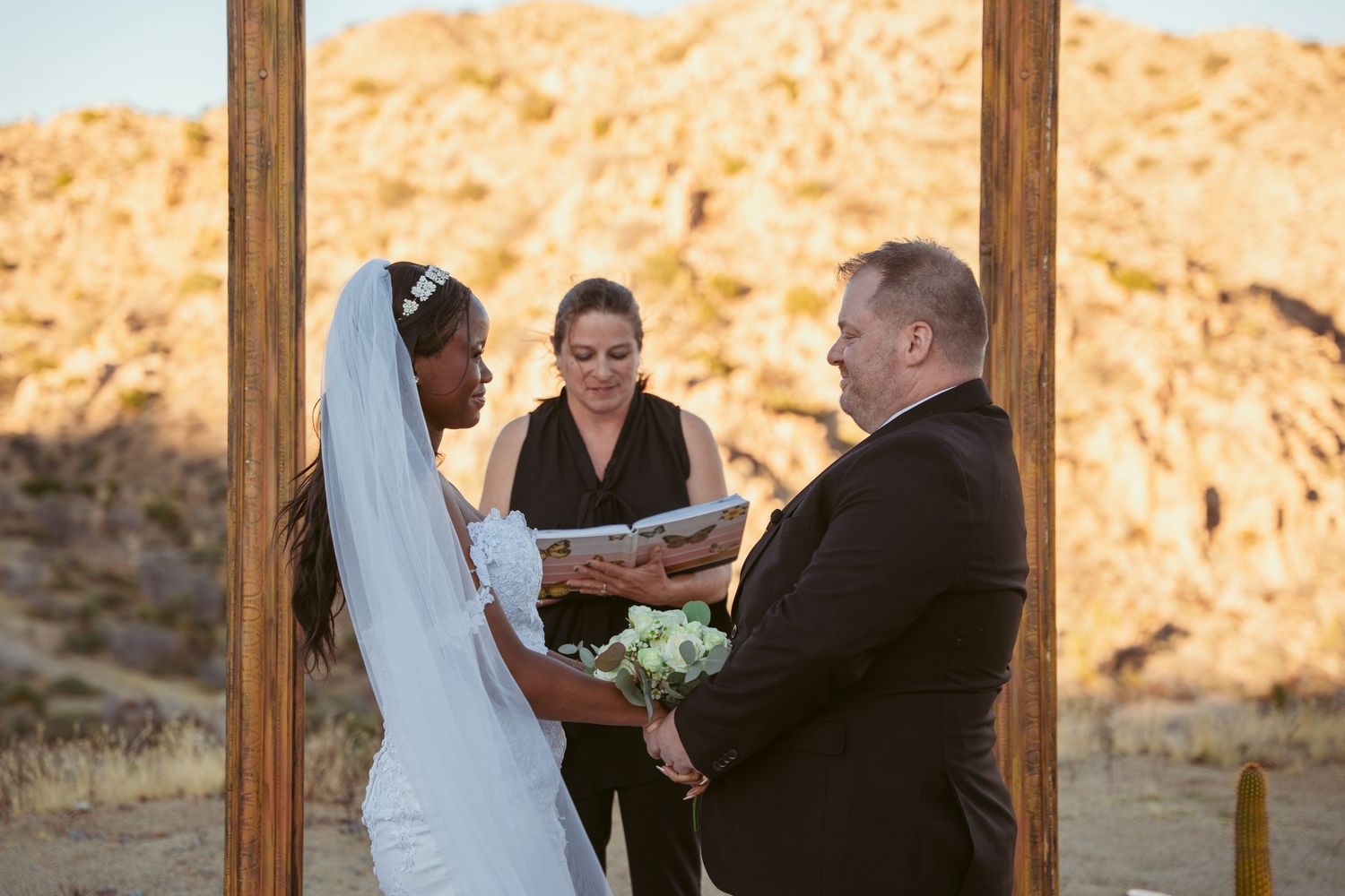 Wedding vows being exchanged under wooden arch in desert landscape.