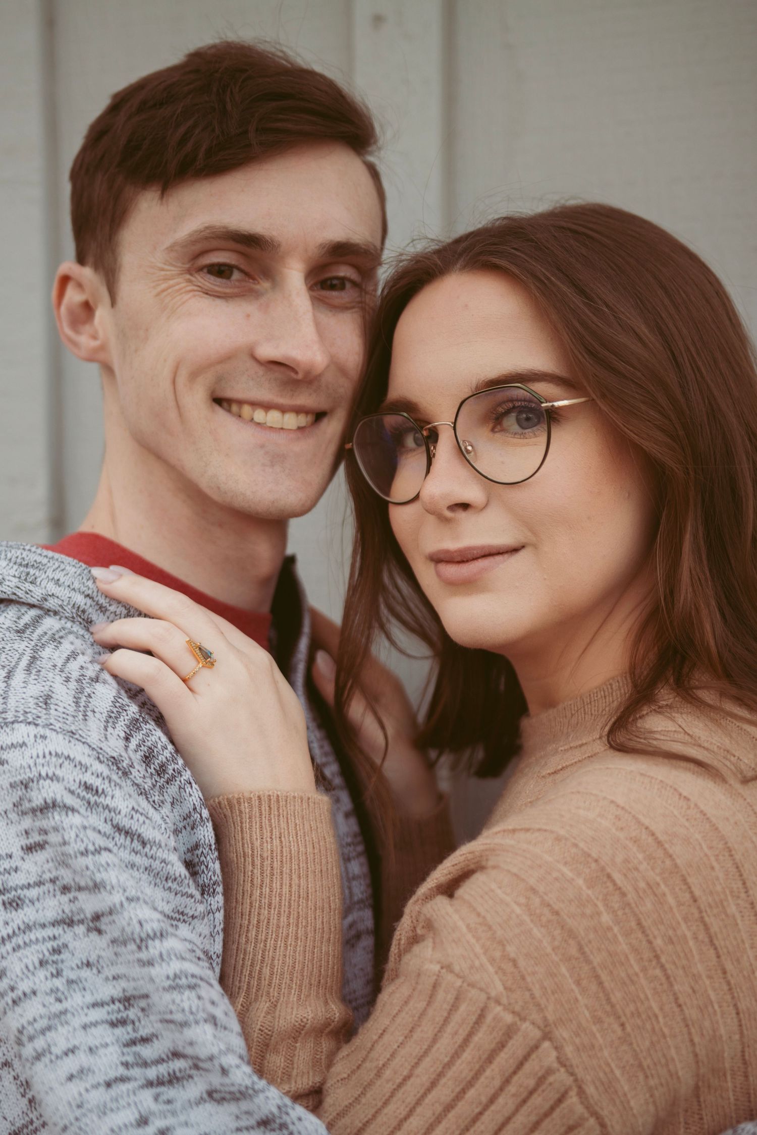 A couple in casual sweaters pose together while smiling warmly at the camera.