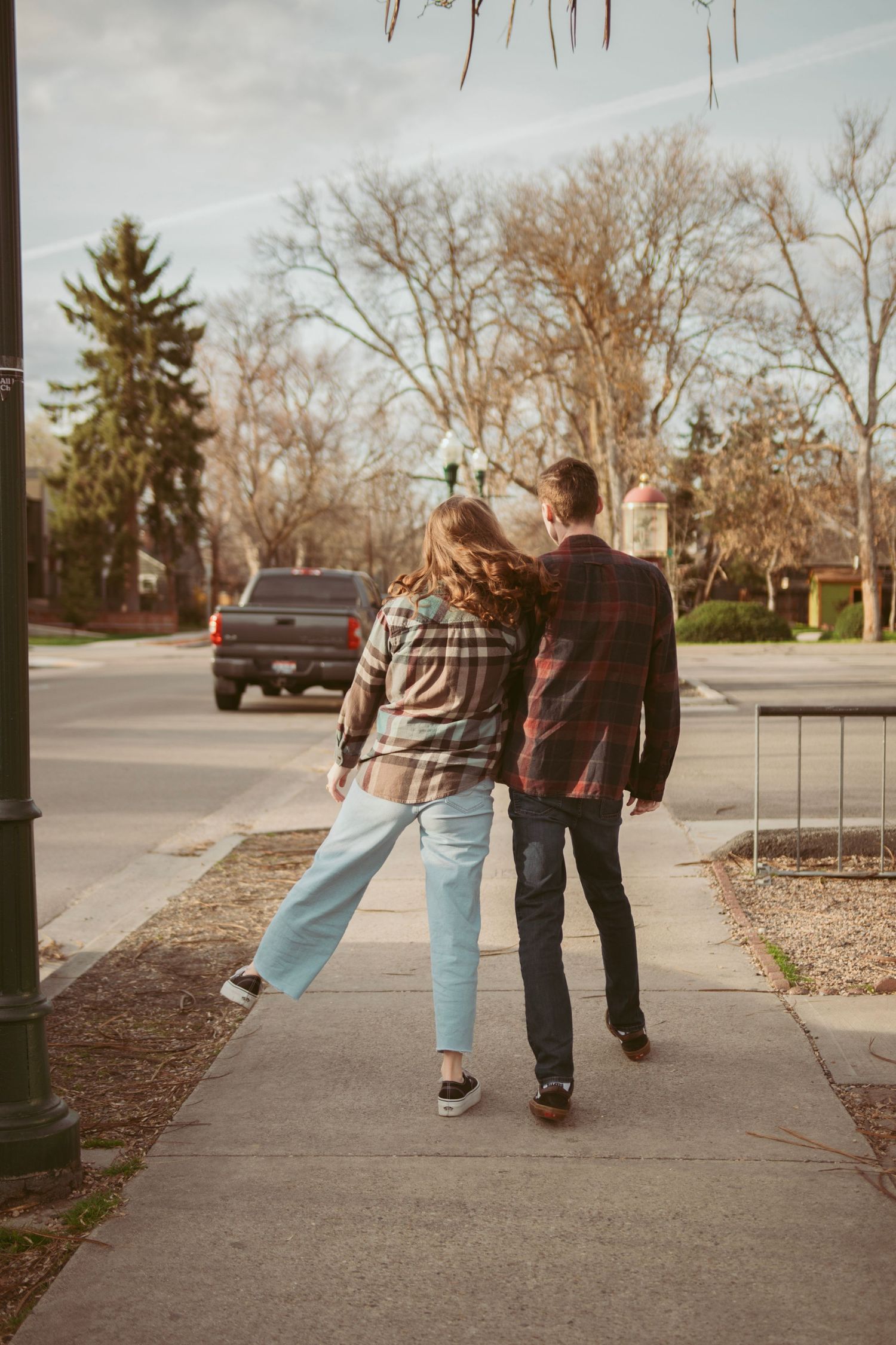 Two people stroll casually down a tree-lined suburban sidewalk at sunset.