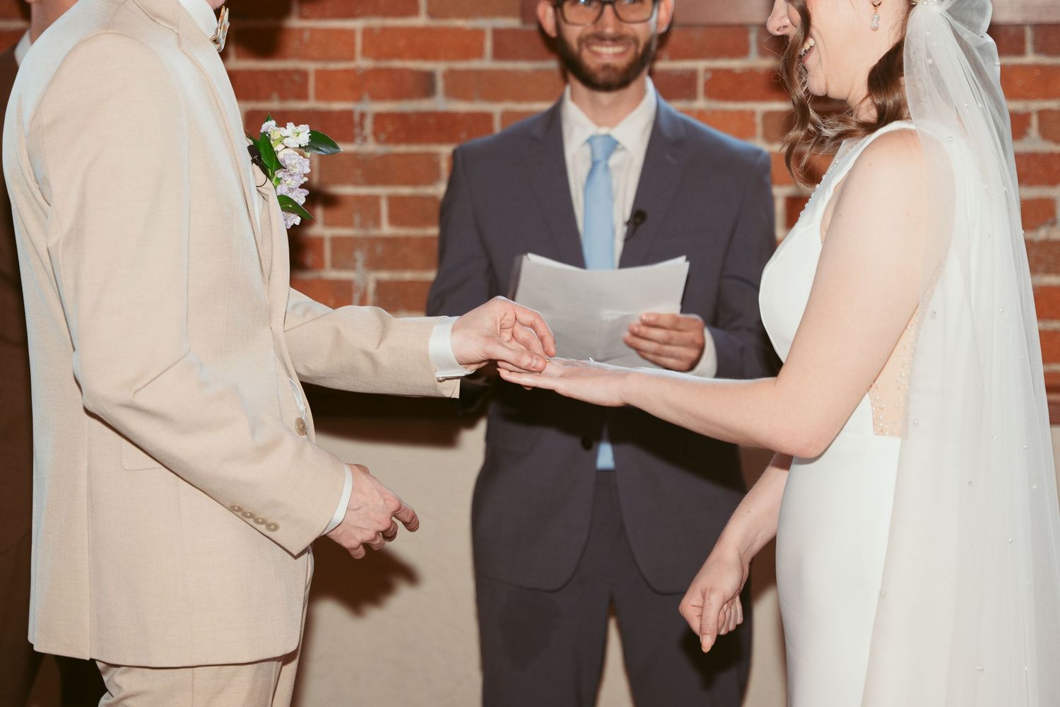 Wedding ceremony taking place in a rustic brick-walled venue with natural lighting streaming through windows.