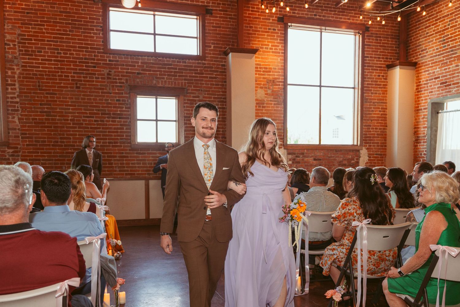 Wedding guests gathered in an industrial-style brick venue with string lights overhead.