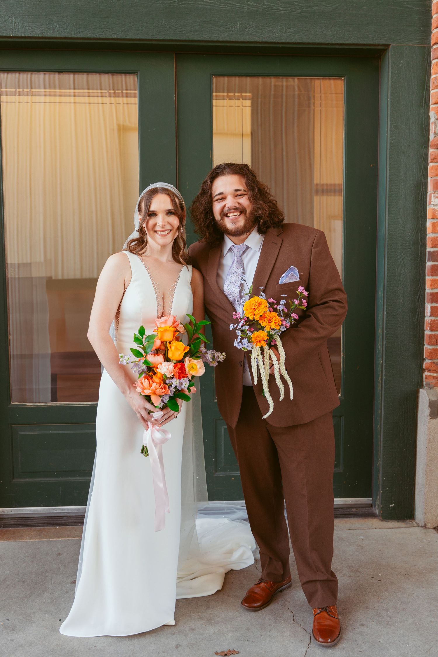 A wedding portrait of a couple in brown suit and white dress holding colorful autumn bouquets.