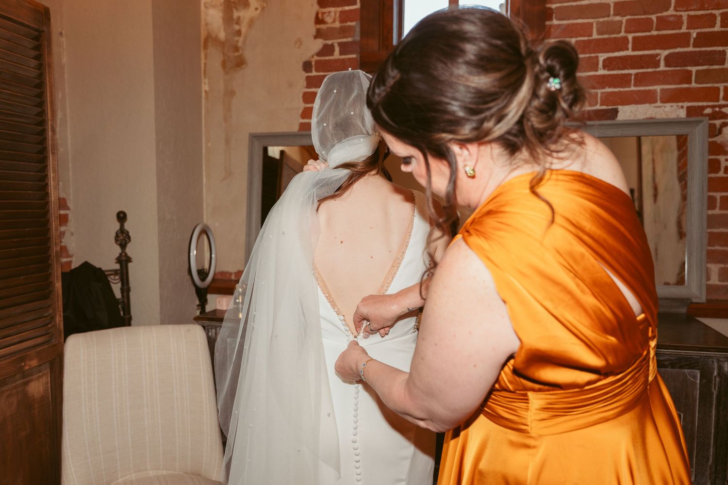 Wedding preparations taking place in a warmly lit room with exposed brick walls.