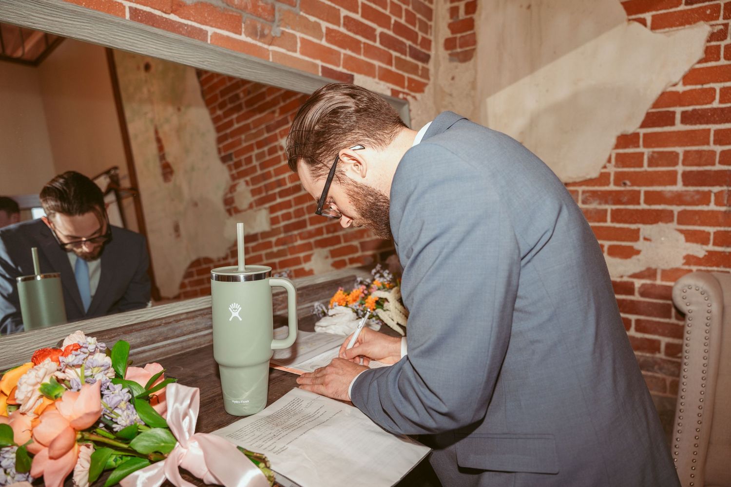 Wedding reception dining setup with colorful floral arrangements against exposed brick walls.