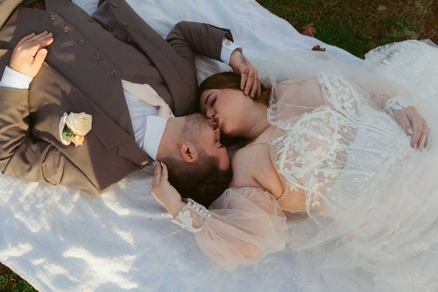 Intimate wedding couple moment captured on blanket in outdoor vineyard setting.