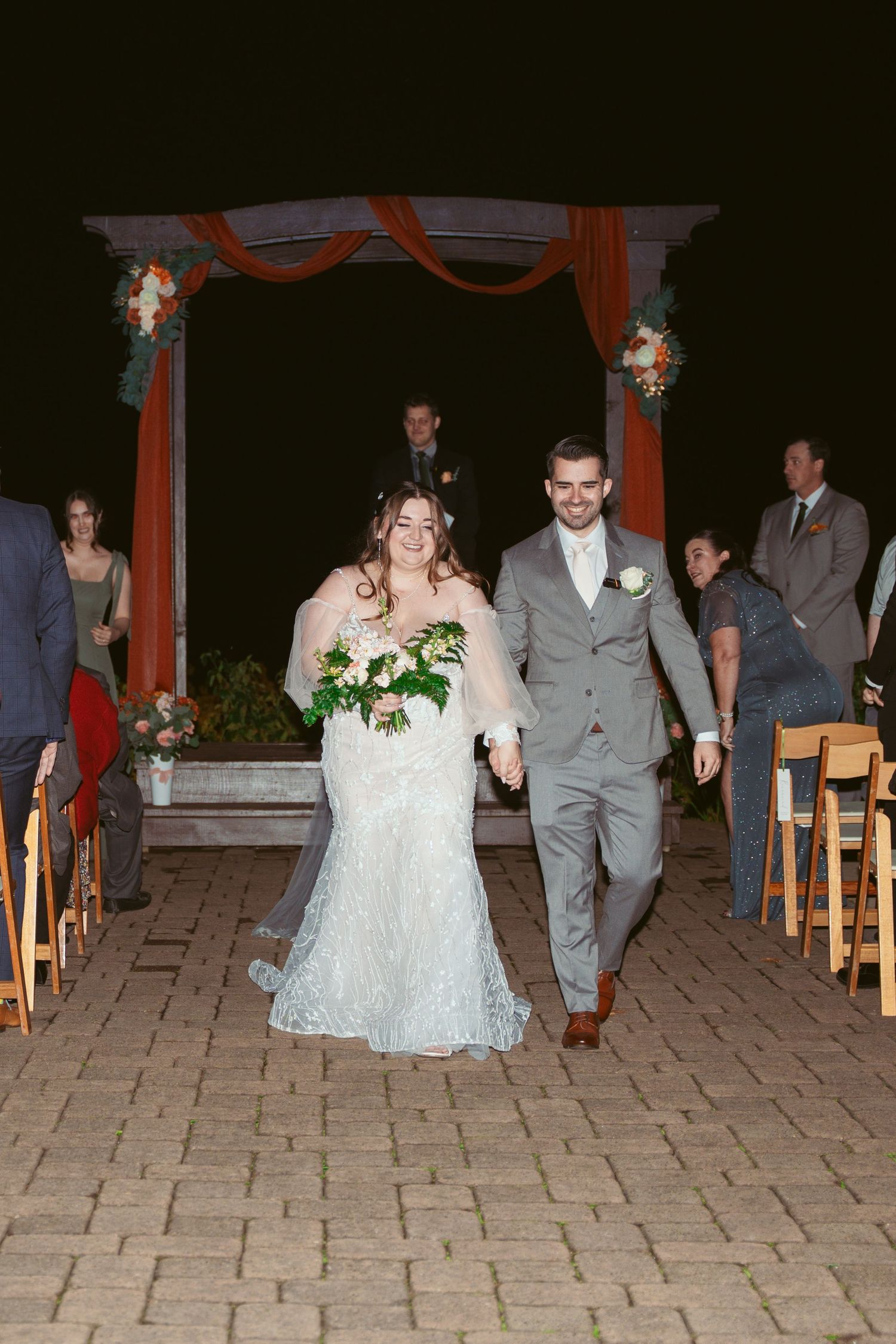 Newlyweds walking down the aisle under a decorated arch at their evening ceremony.