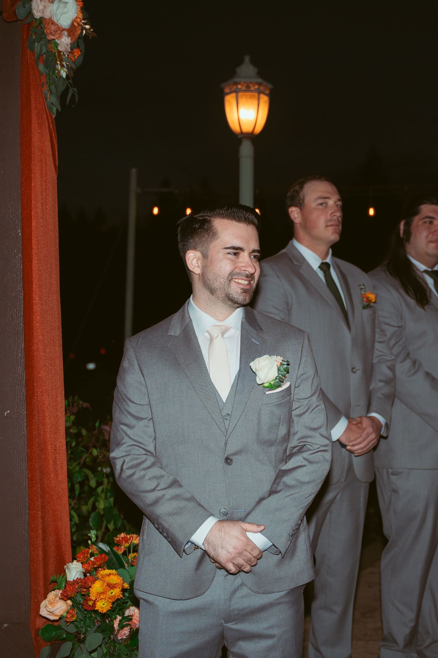 Wedding party members in gray suits gather near decorative orange lanterns.