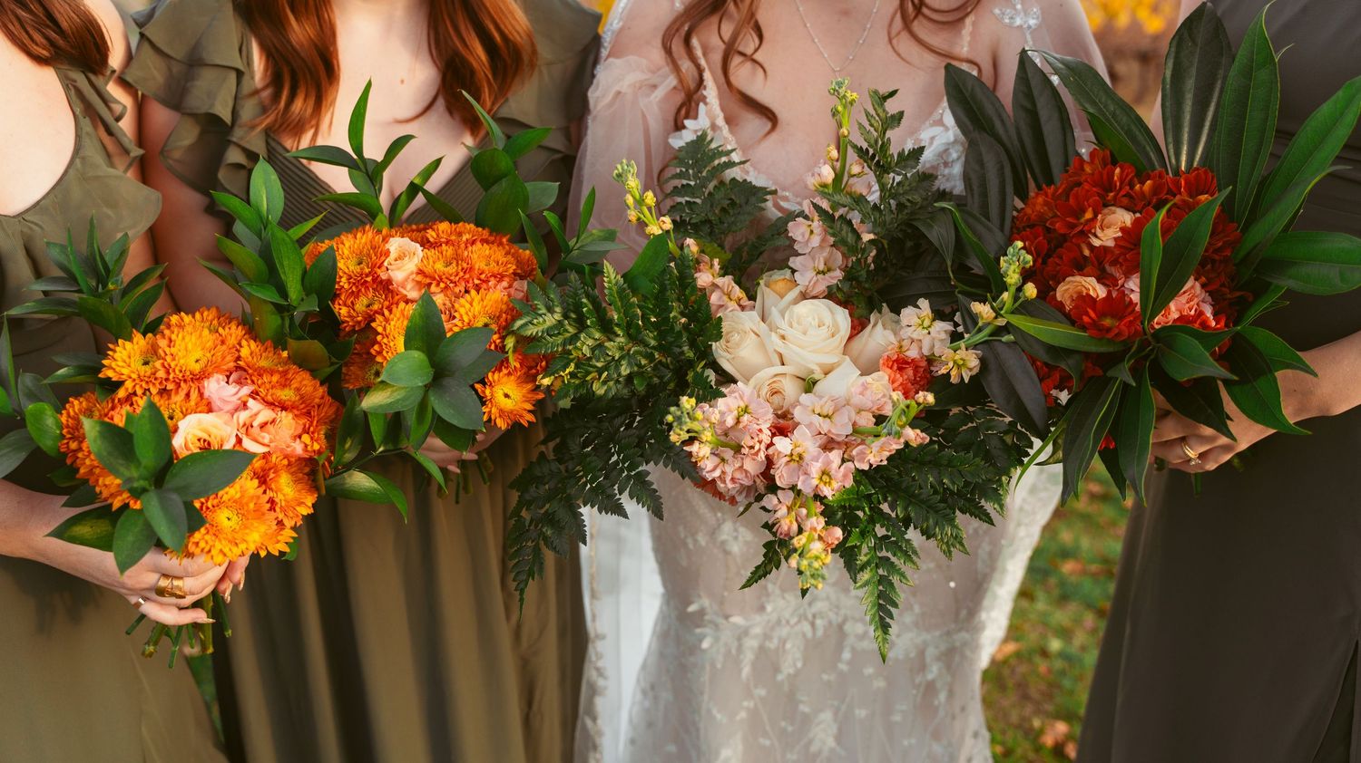 Colorful orange and pink wedding bouquets with mixed flowers and greenery held against formal attire.