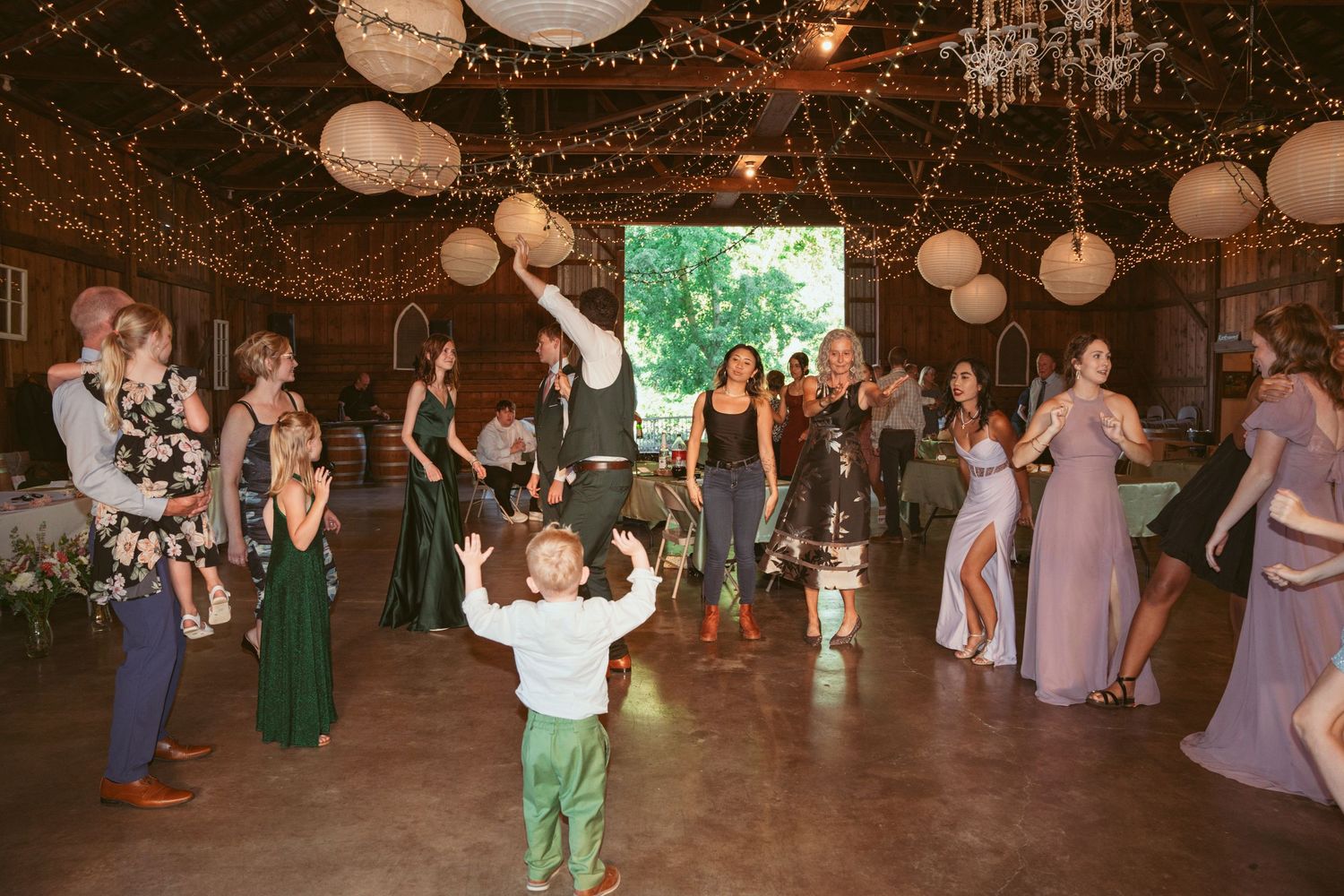 Energetic dance party at a barn wedding reception with string lights and paper lantern decorations.