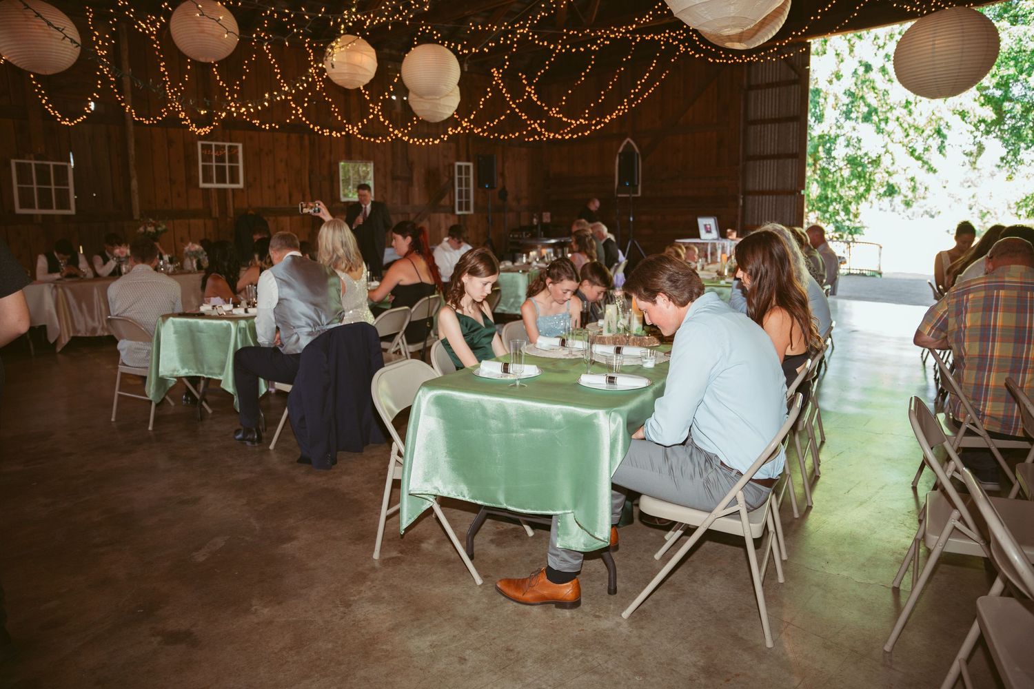 Rustic barn wedding reception venue decorated with white paper lanterns and string lights.