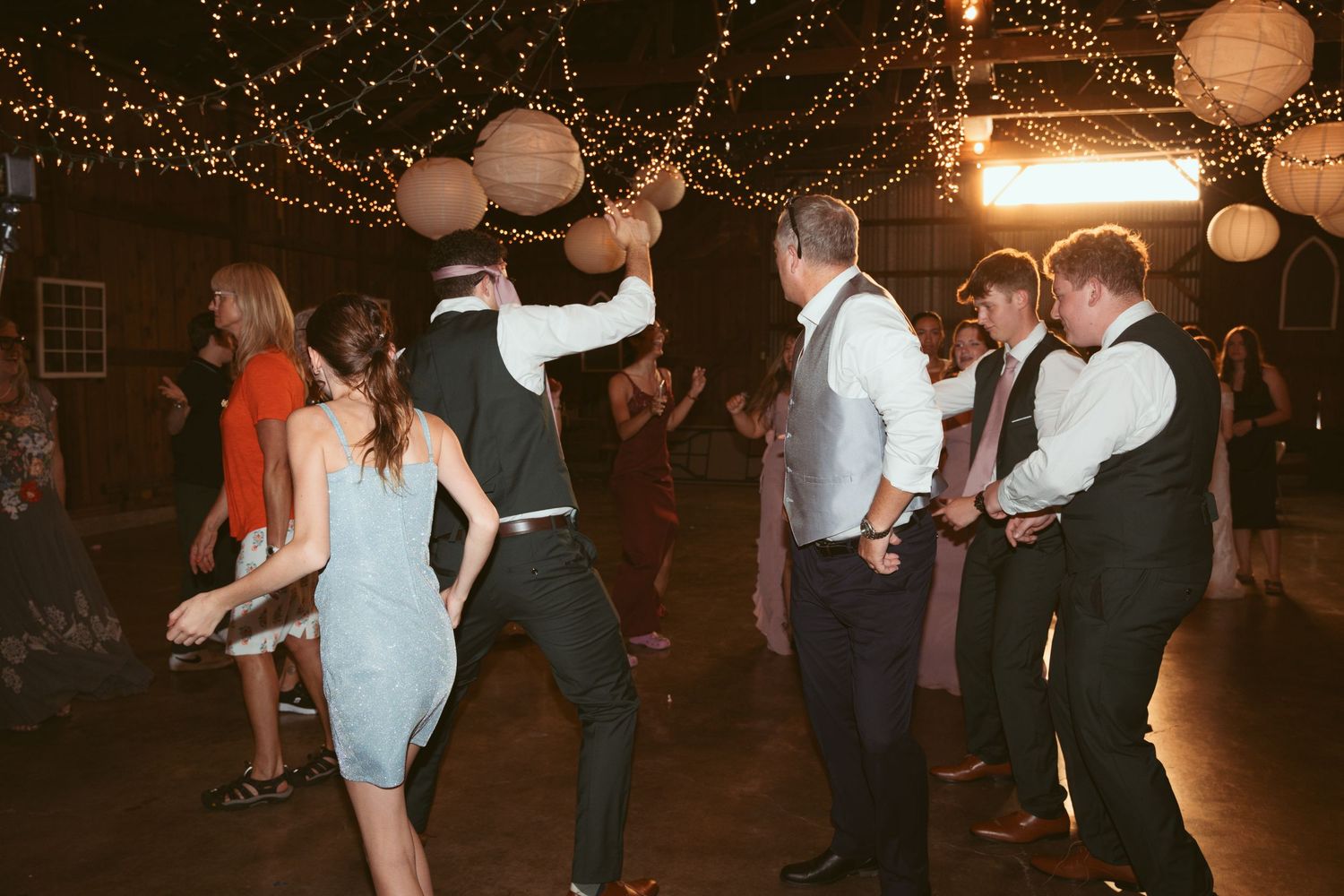Couples dancing together at a festive barn party with string lights and lanterns.