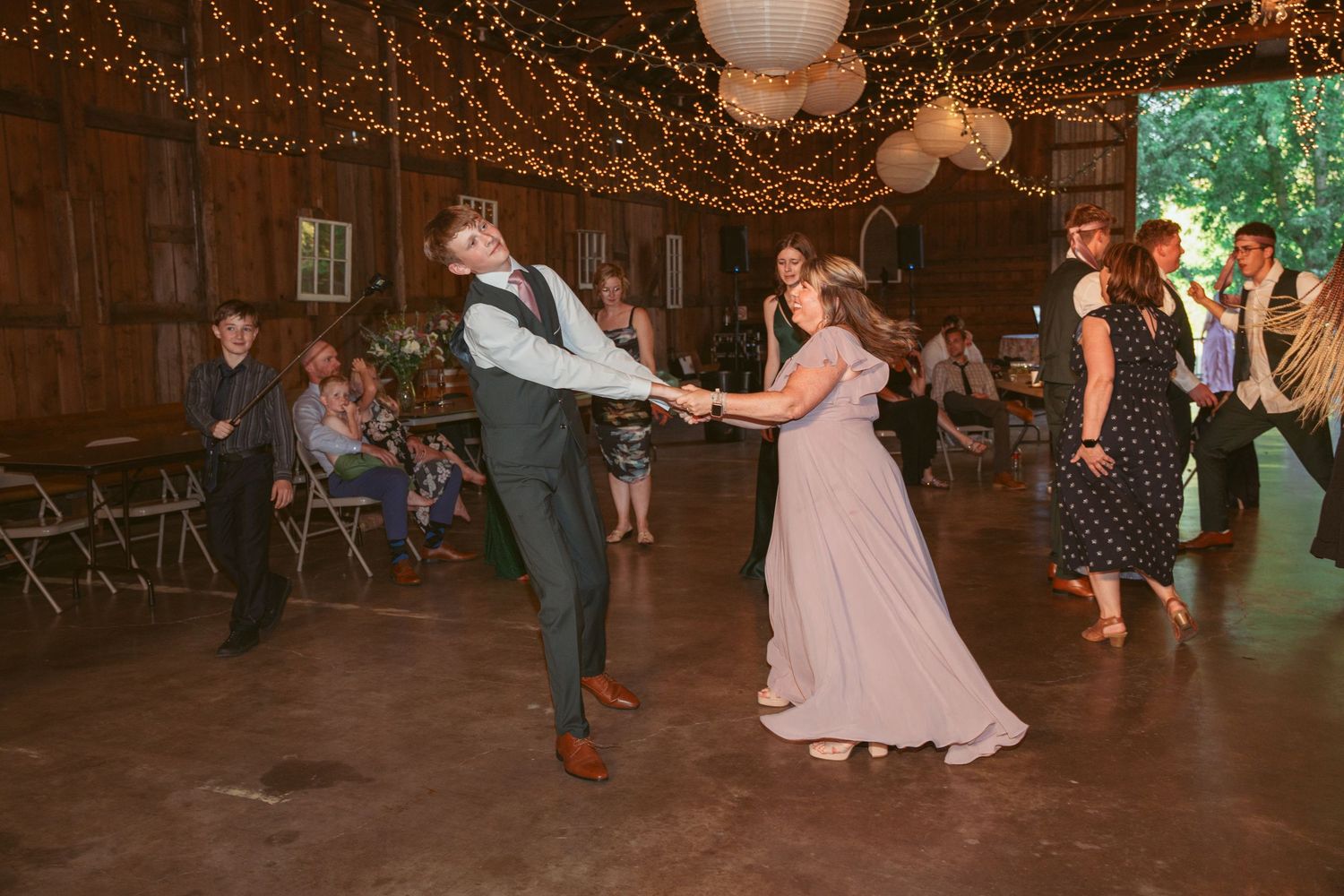People dancing and twirling on wooden dance floor under decorative string lights.