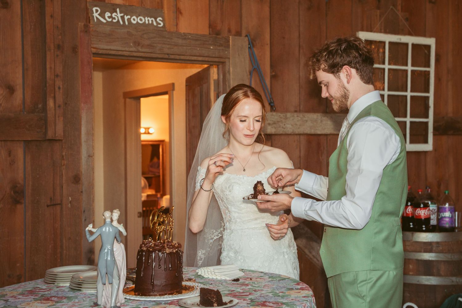 Wedding couple feeding each other cake in a rustic barn venue with wooden walls.