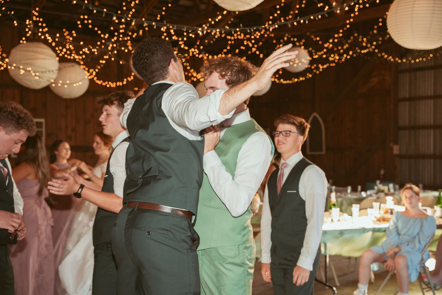 Festive barn wedding reception with string lights and dancers on the wooden floor.